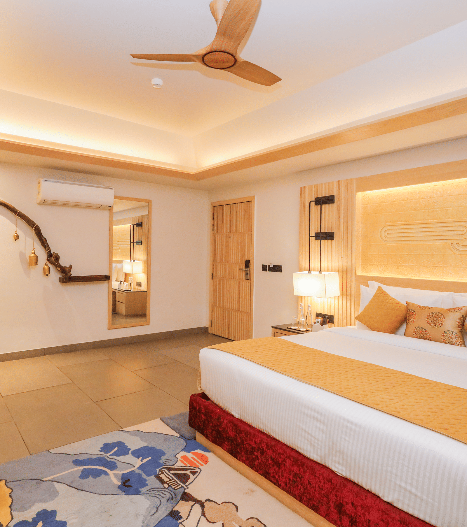 A room with a double bed, ceiling fan, seating and wall features arranged around a central area at Ananta Spa & Resort, Jaipur.