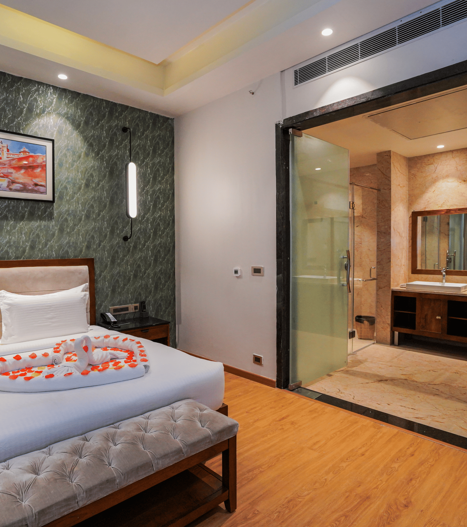 A room with a bed decorated with petals and an attached glass-walled bathroom at Pushkara Resort & Spa.
