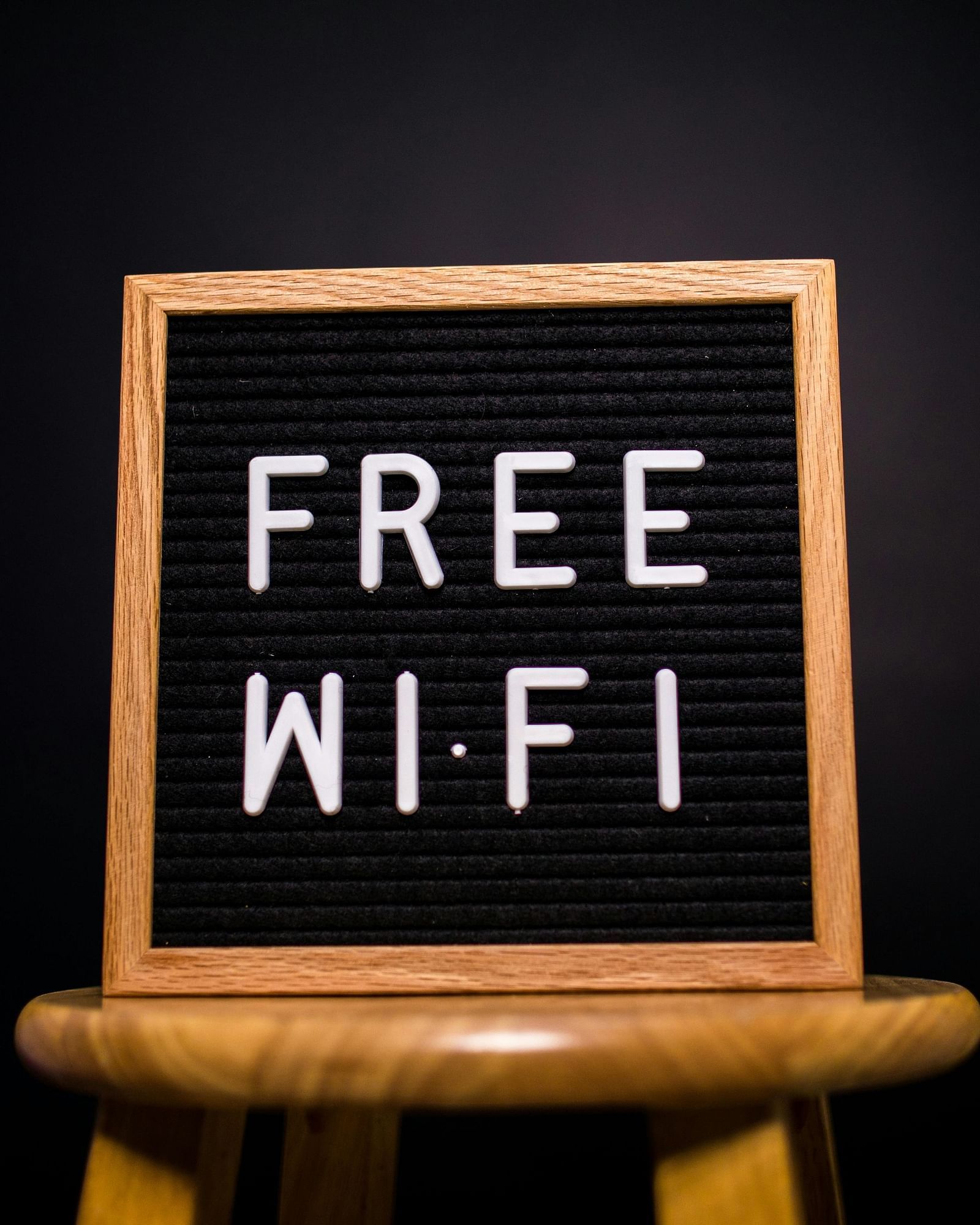 A black letter board with white text reads FREE WI-FI and rests on a small wooden stool against a dark background.
