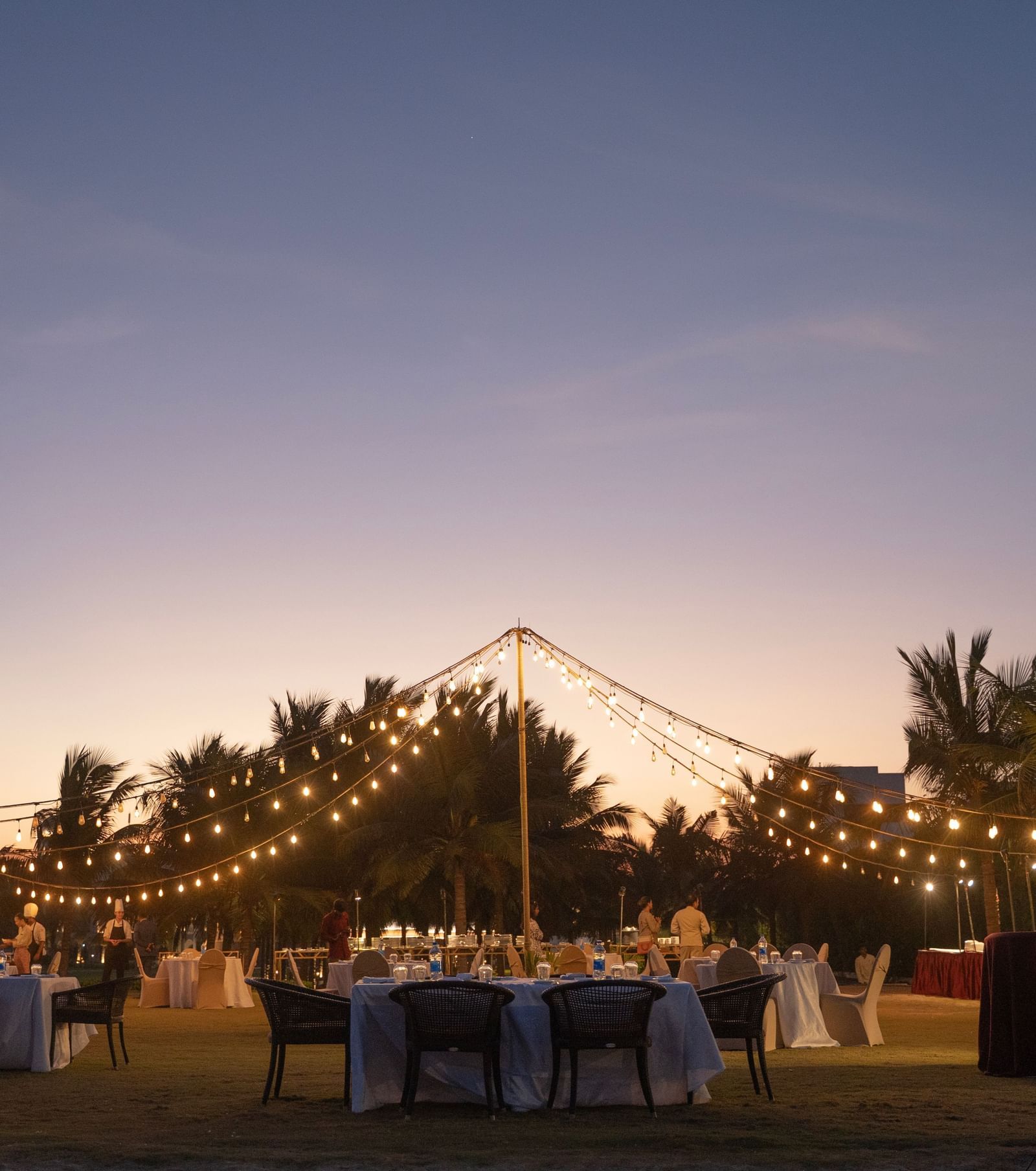 Outdoor evening event setup with string lights and a sunset backdrop - Kaldan Samudra Palace