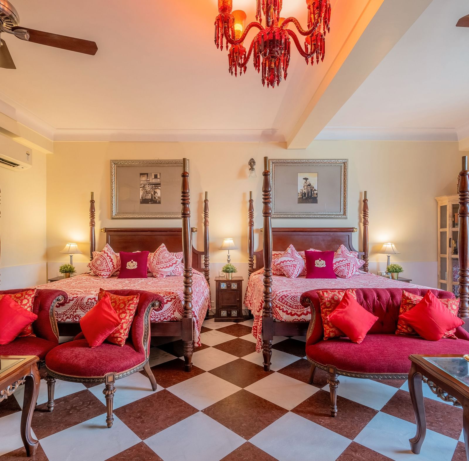 A spacious suite at Dera Rawatsar, Jaipur, features two elegant four-poster beds, comfortable seating areas, ornate tables, and a striking checkered floor.