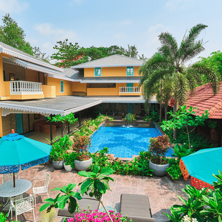 Courtyard view of MAYFAIR Alibaug featuring a turquoise swimming pool and bright yellow Mediterranean-style buildings.