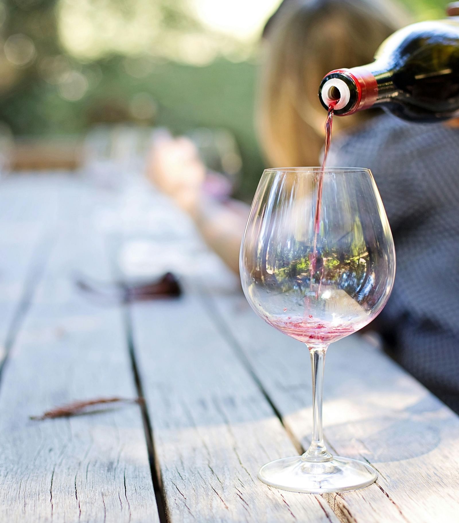 Wine being poured by a staff member into a glass that is kept on a wooden table.