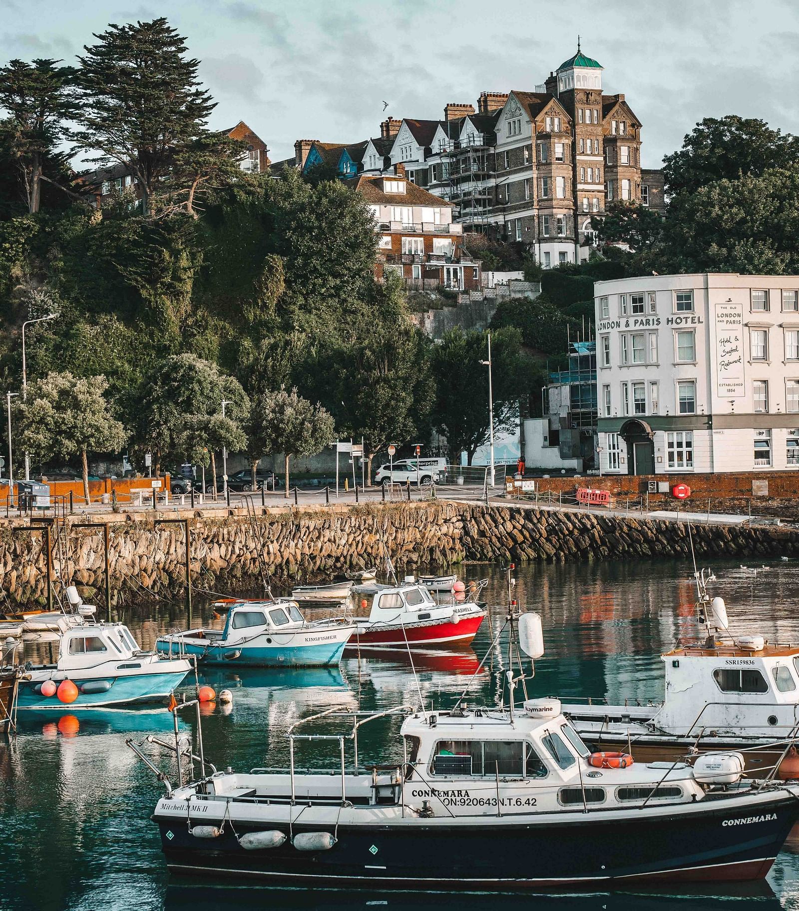 An overview of a marina with many boats parked on the waterbody and building in the background.