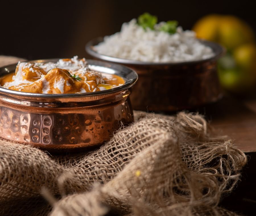 Traditional Indian dish of paneer butter masala served in a copper bowl, paired with steamed rice in a rustic, warm setting.