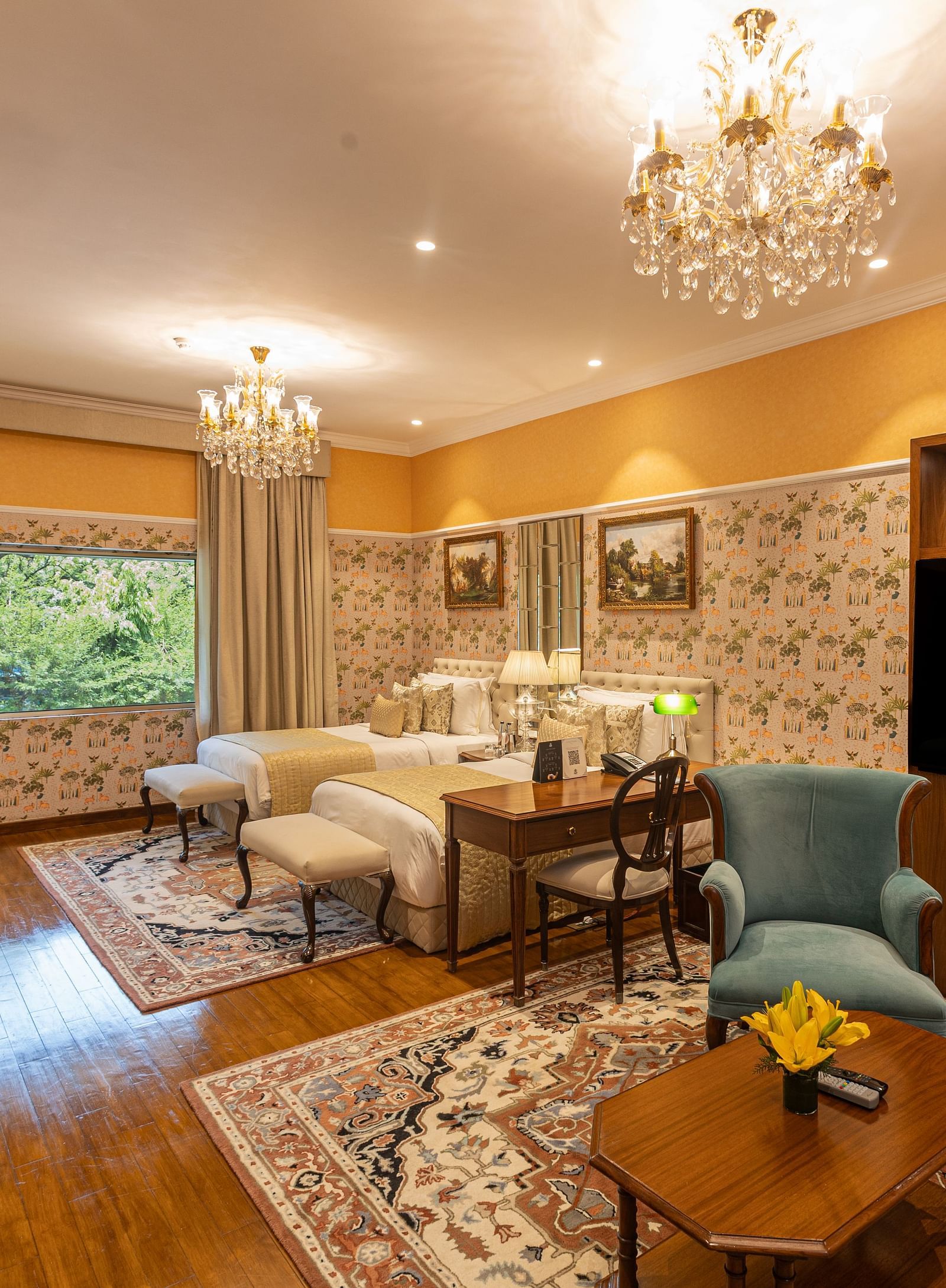 Grand Luxury Twin Bed Room at The Claridges New Delhi, featuring twin beds with chandeliers hanging above and a large glass window offering a scenic view