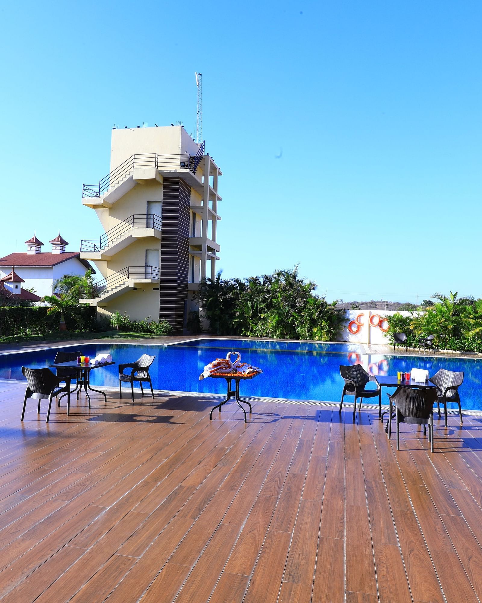 A large swimming pool with sun loungers and umbrellas, surrounded by greenery - Vishal Lords Inn Gir Forest