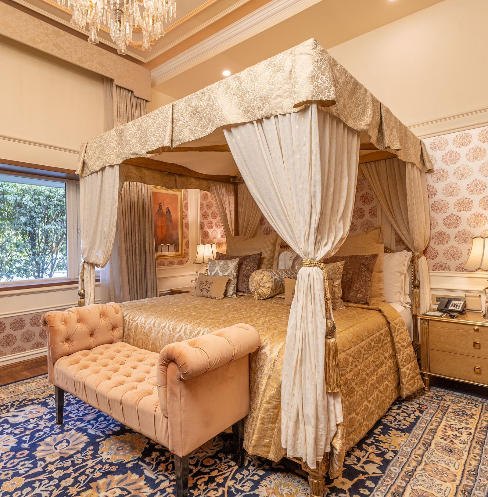 Executive Suite at The Claridges New Delhi, featuring a charming canopy bed, a sofa at the foot, bedside lamps, and a serene view through the window