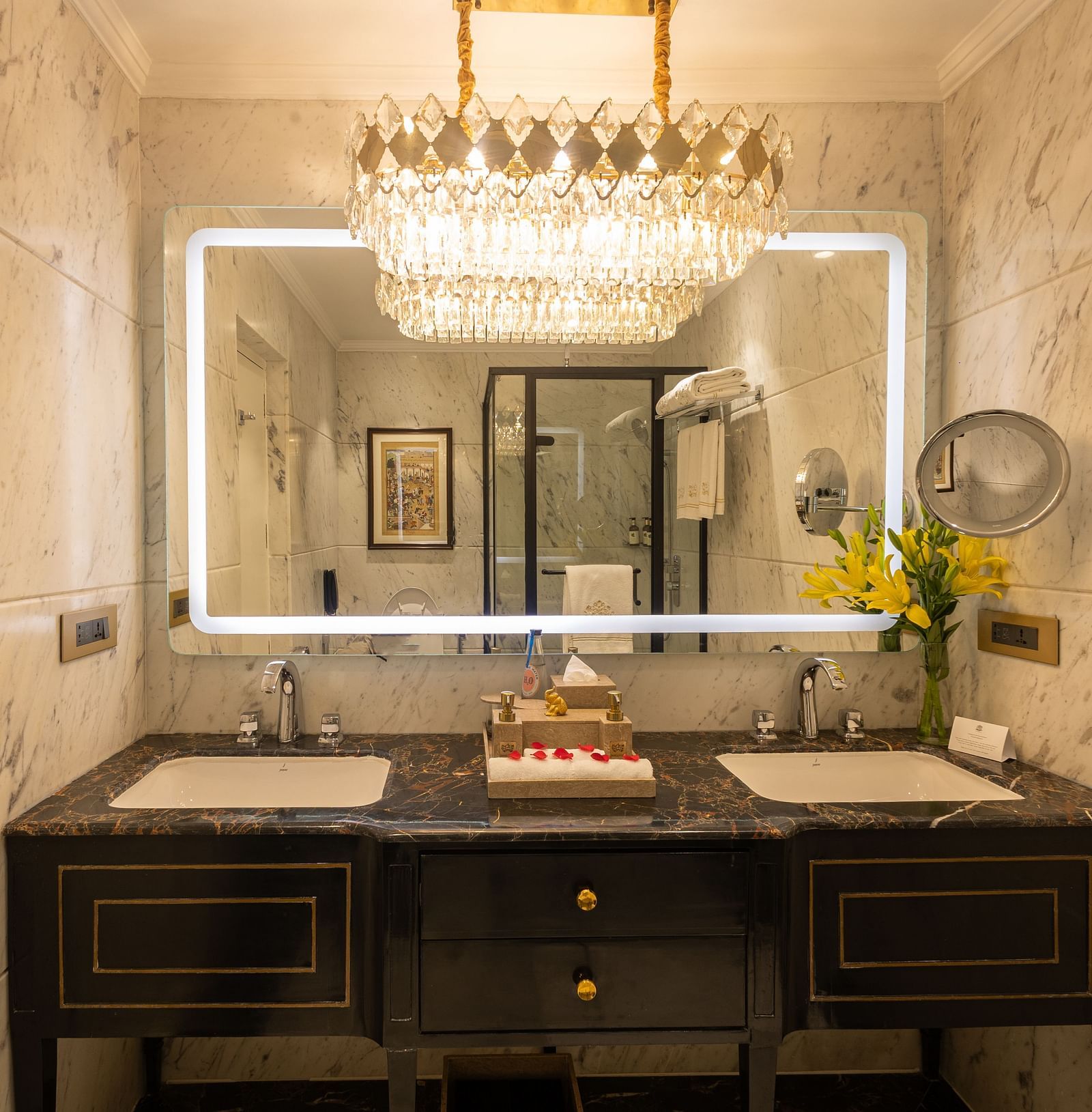Washroom of the Grand Luxury Twin Bed Room at The Claridges New Delhi, featuring sinks, a wall-mounted mirror, and an elegant chandelier hanging above