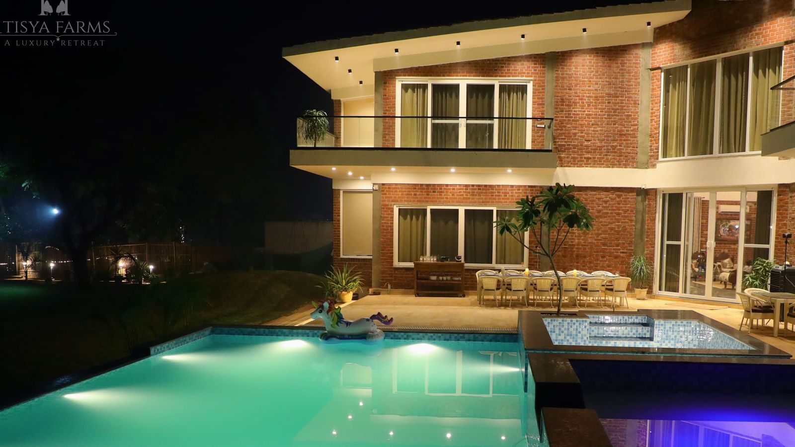 A night view of a farmhouse with an illuminated swimming pool in front at Tisya Farms, Gurgaon.
