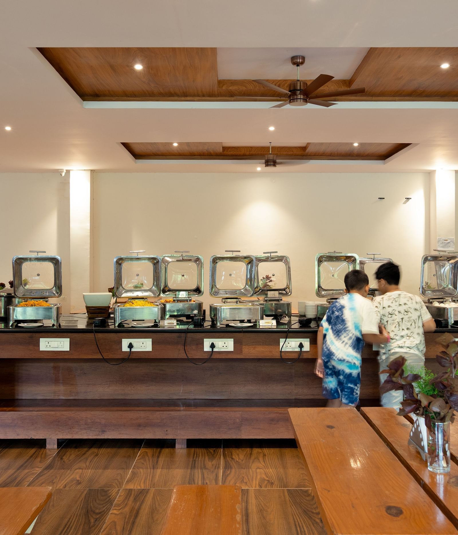 A well-lit indoor dining area features a buffet setup with multiple food warmers and a few people present | Lake View Restaurant