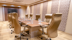 A well-lit boardroom featuring a long wooden table with multiple swivel chairs, a wall-mounted television, and patterned wall panels | Pride Elite Chhatrapati Sambhajinagar