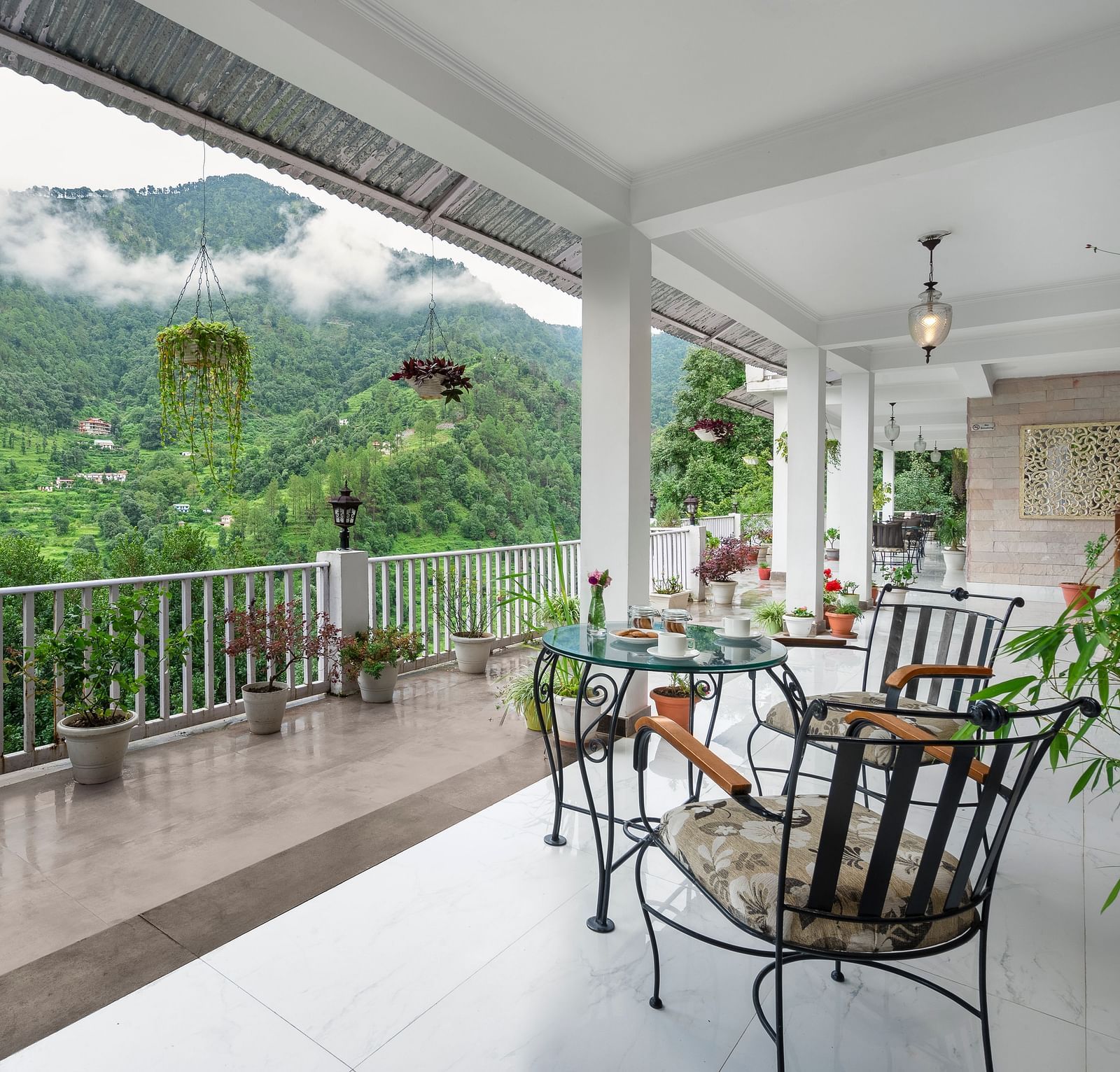 An image of a courtyard filled with flower pots and at the centre there is are three chairs and a table - Suvaasa, Ramgarh 