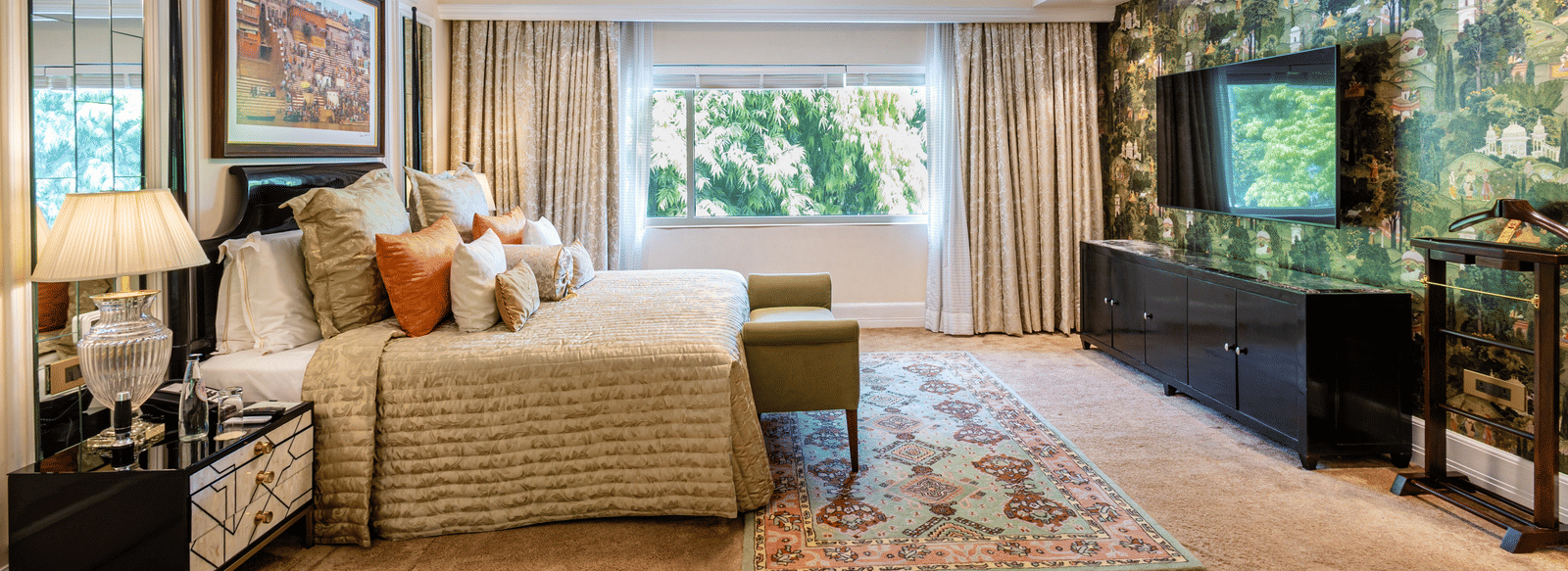 Presidential Suite bedroom featuring a sofa, armchair, coffee table, television, floor lamp, and large windows overlooking greenery at The Claridges New Delhi.
