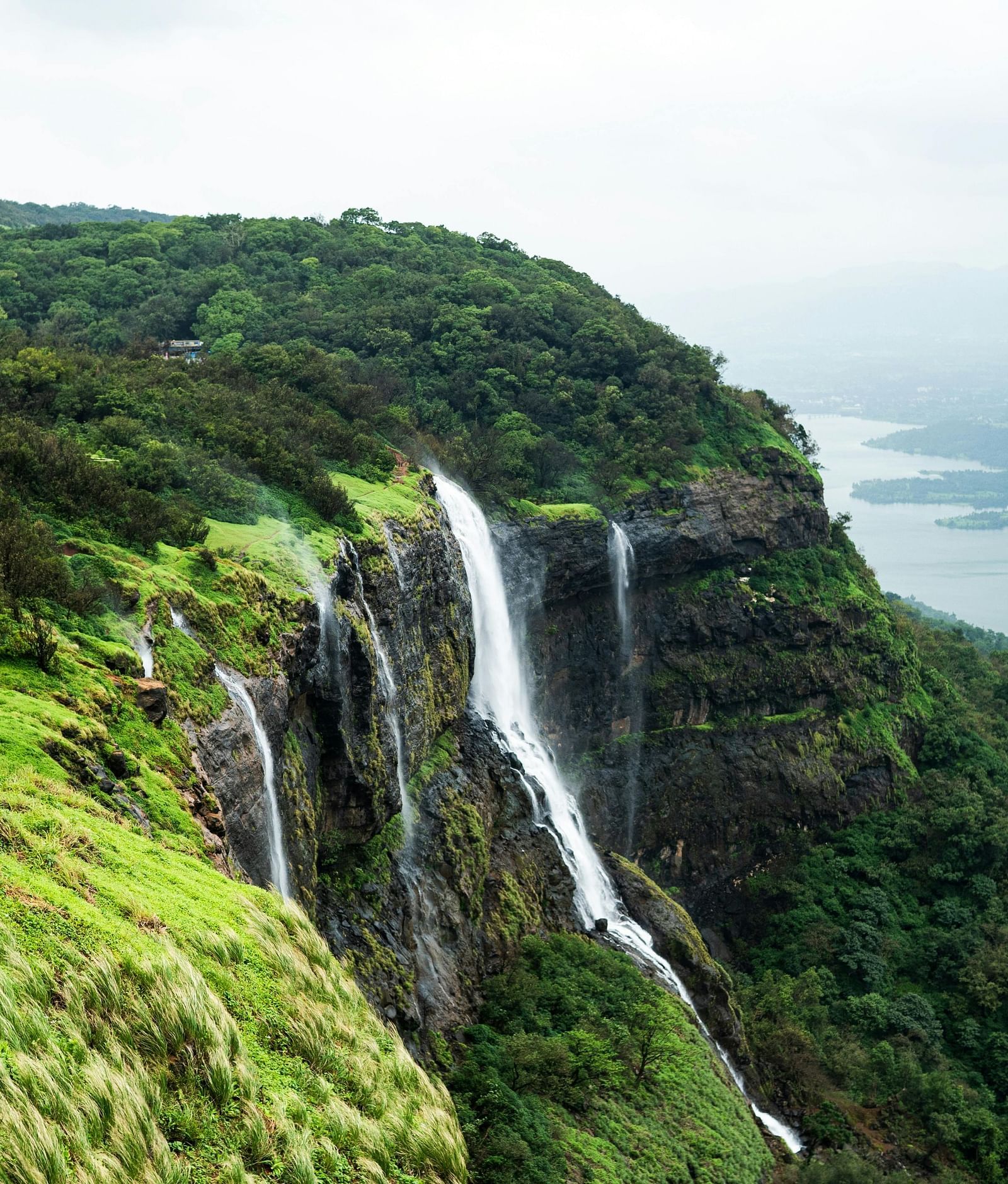 A waterfall surrounded by lush greenery is seen from the top of a mountain.