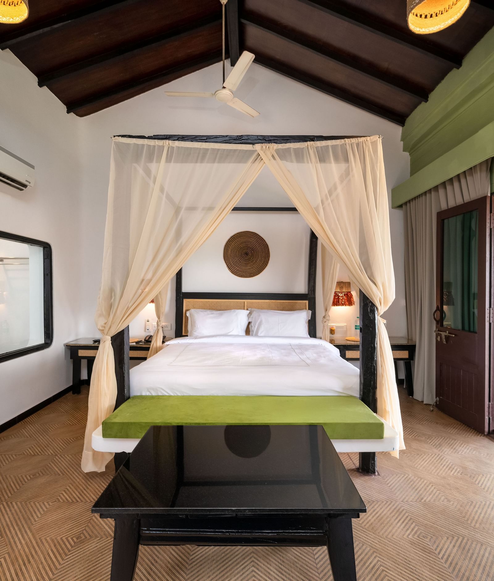 Elegant bedroom with a canopy bed, vibrant green accents, artistic wall decor, and a seating area opening to a private patio with outdoor seating