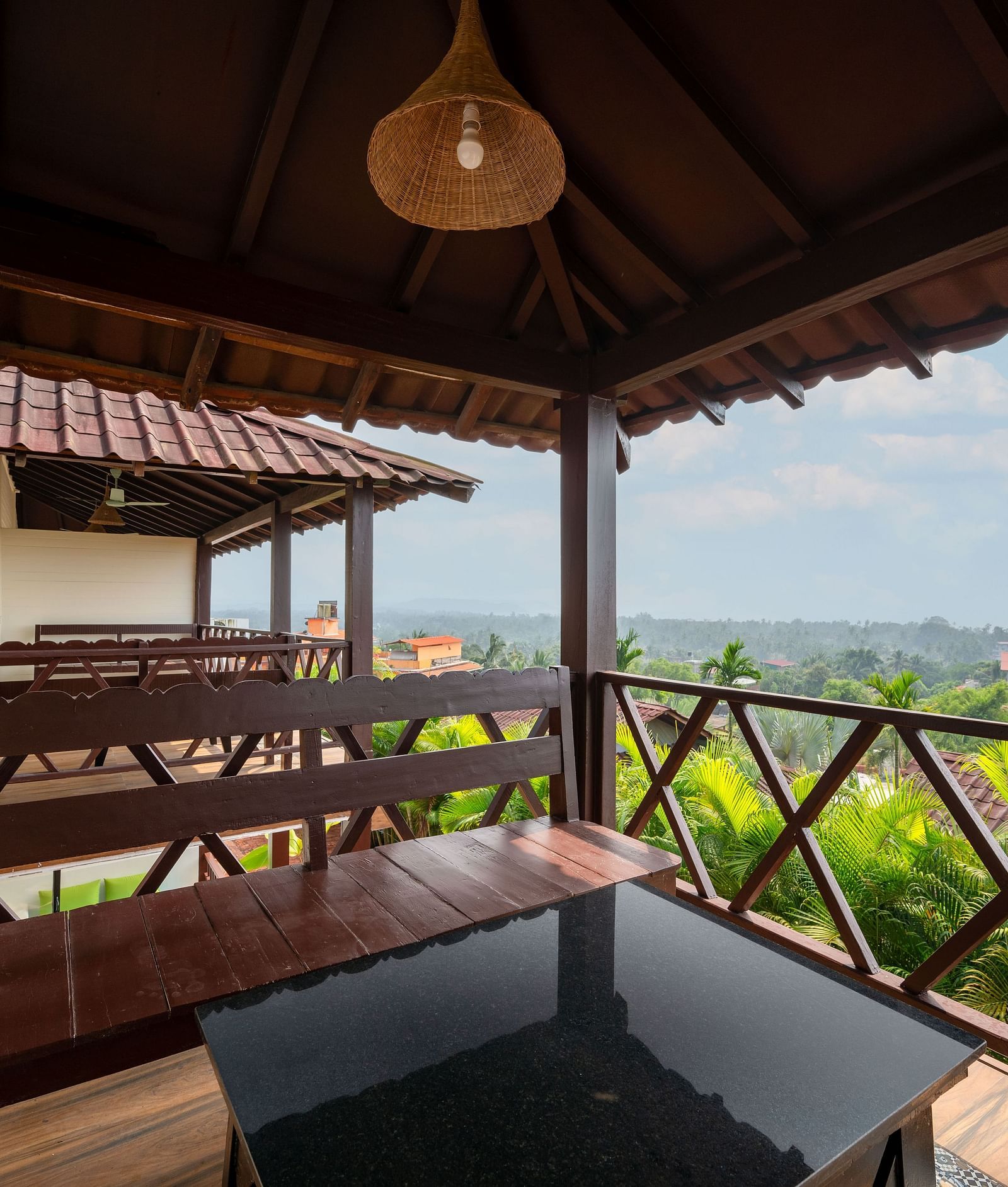 An image showing a balcony view with greenery, shot from a room with wooden details and benches