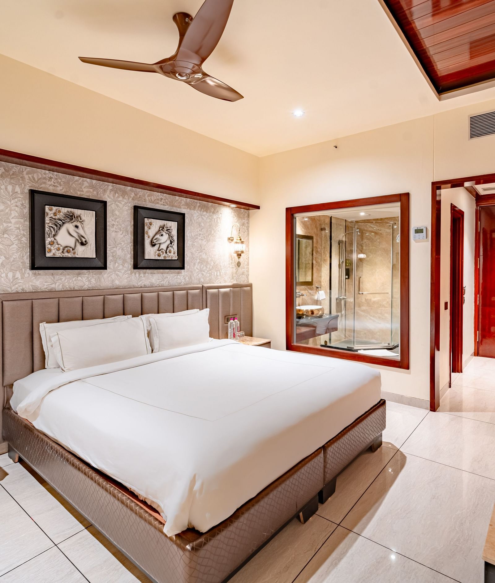 A spacious bed with two photo frames above, a bedside table with essentials, and a wall mounted TV opposite at  Crescent Spa & Resort, Indore