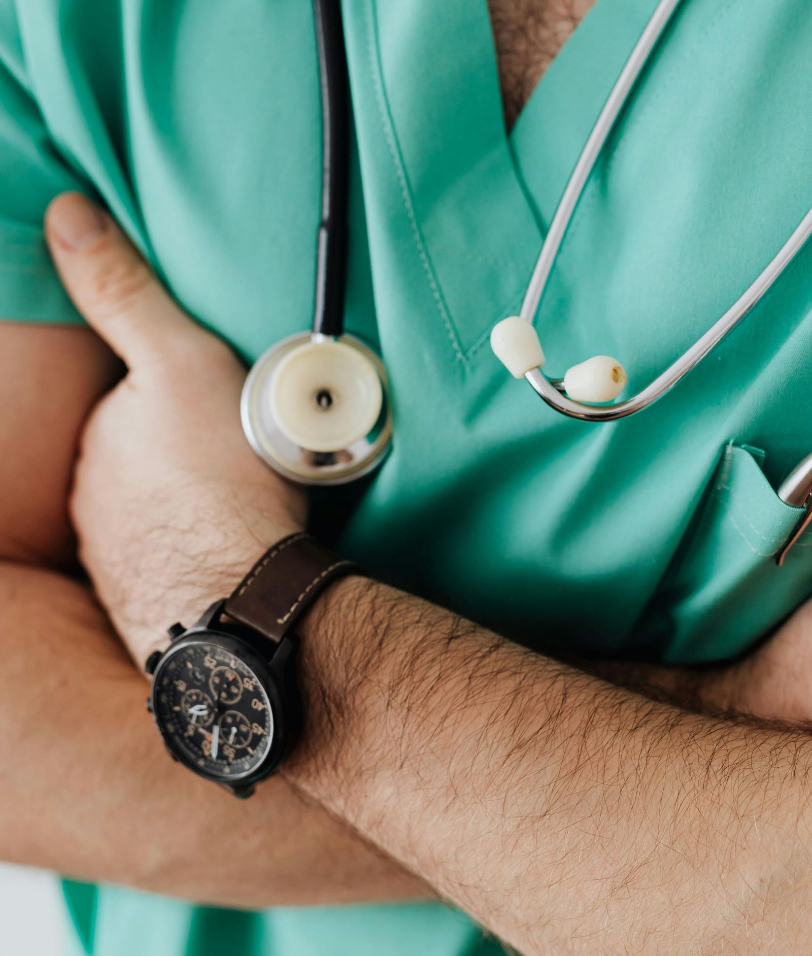 A person in green scrubs with a stethoscope around their neck, standing with their arms crossed.