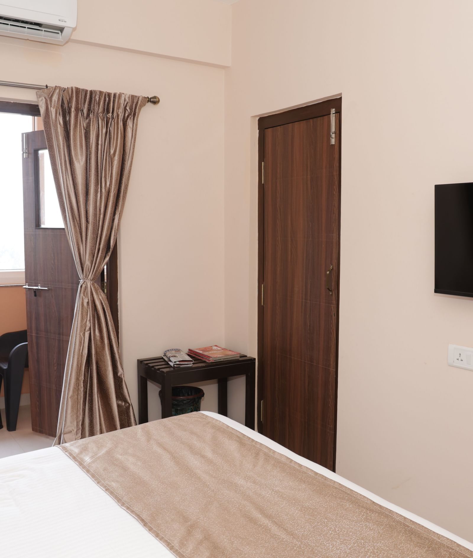 A bed near a window with curtains, a desk, chair and wall-mounted television at Nazri The Verda Hotel, Arambol.