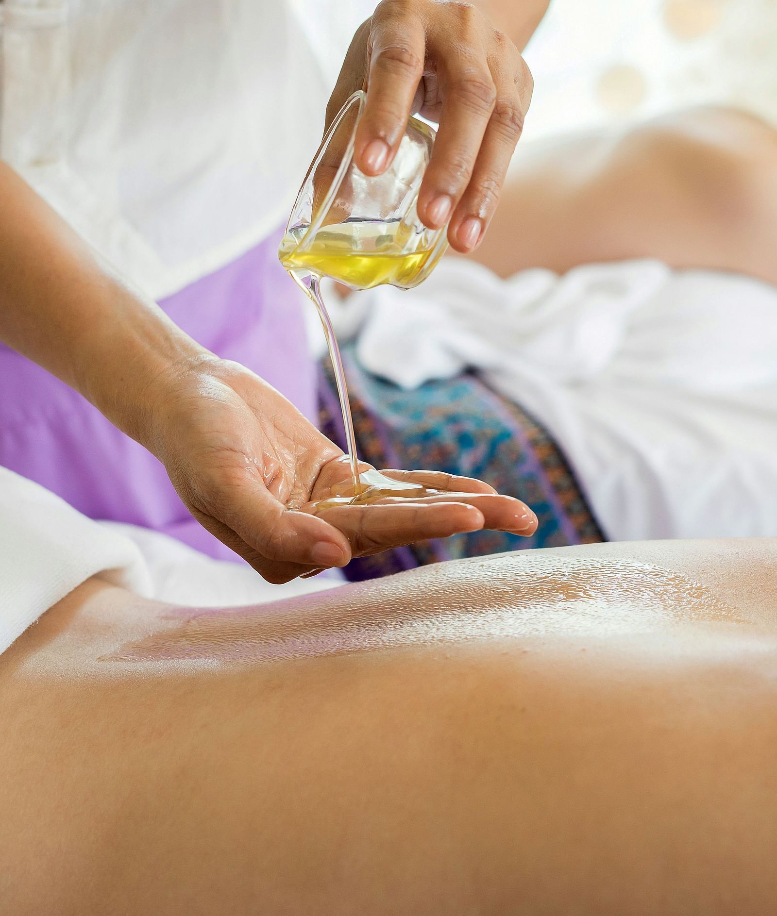 A person receiving an oil massage at a spa, with another person resting in the background.
