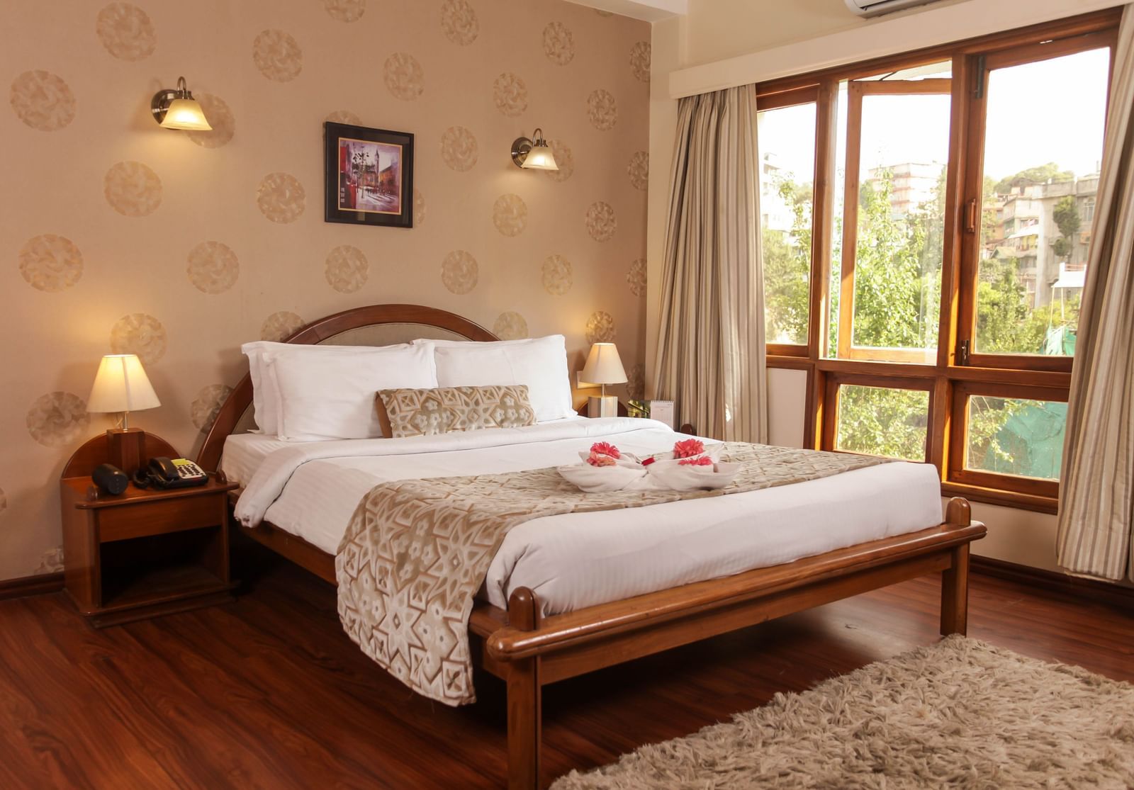 A well-lit bedroom at the Polo Hotel Shillong with a large bed, wooden floors, and a bright window.