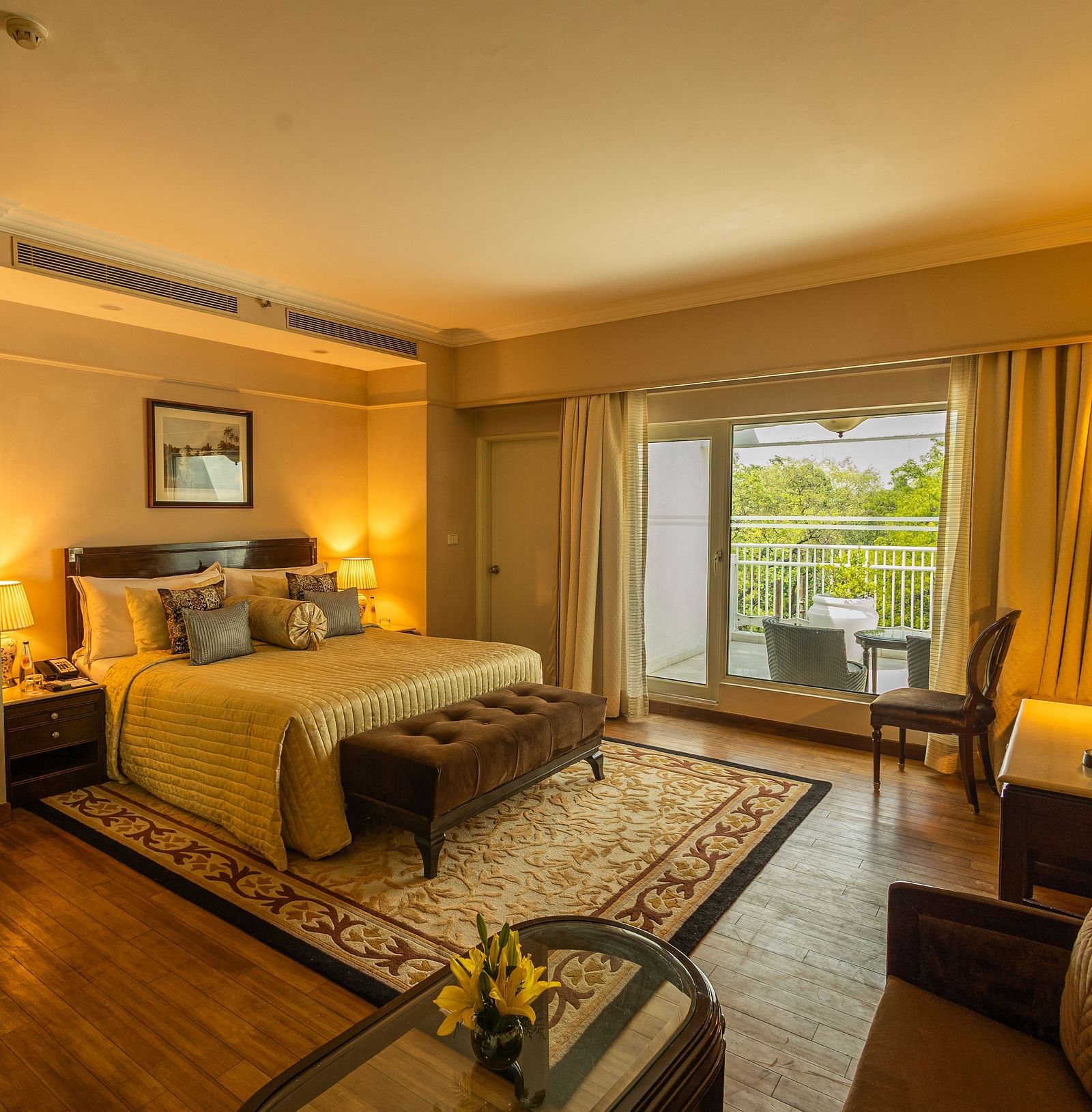 Luxury King Bed Room with Balcony at The Claridges New Delhi, featuring a cosy bed, a framed artwork on the wall, and a glass door to the balcony