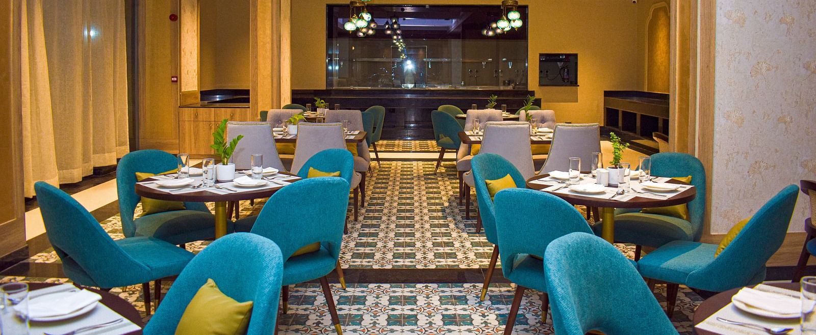A modern restaurant interior with teal armchairs, round tables, patterned tile floor, and a distinctive globe chandelier - Urban Suites by BluSalzz, Jaipur