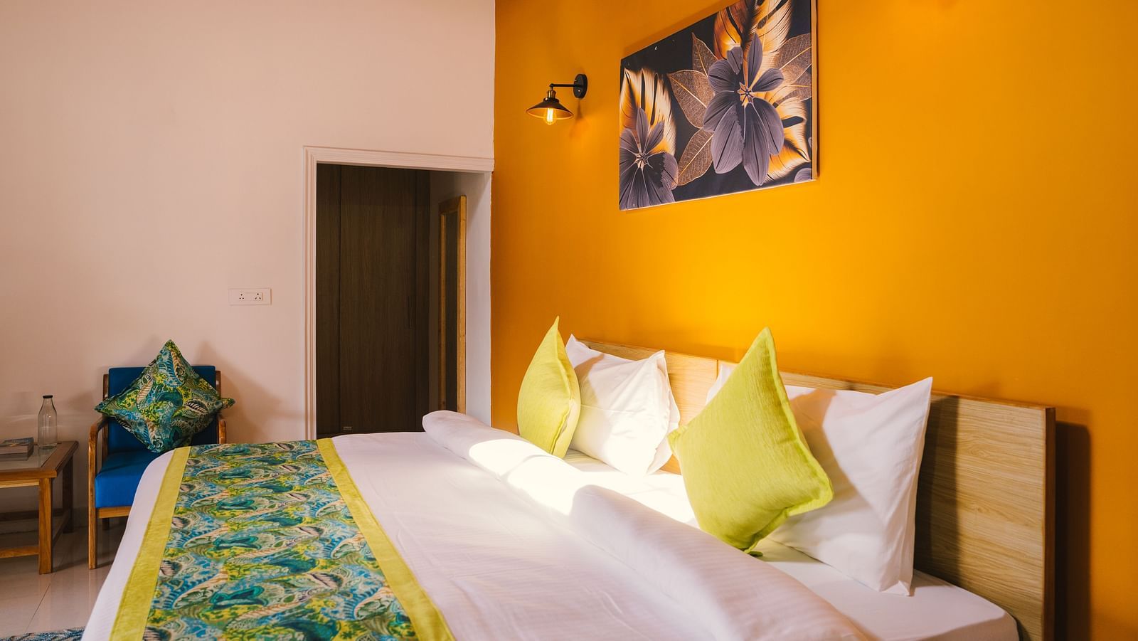 A side view of a neatly made bed with a photo frame above the headboard, two night lamps on either side, and a door in the background at BluSalzz Villas - The Green Roof, Bhimtal.