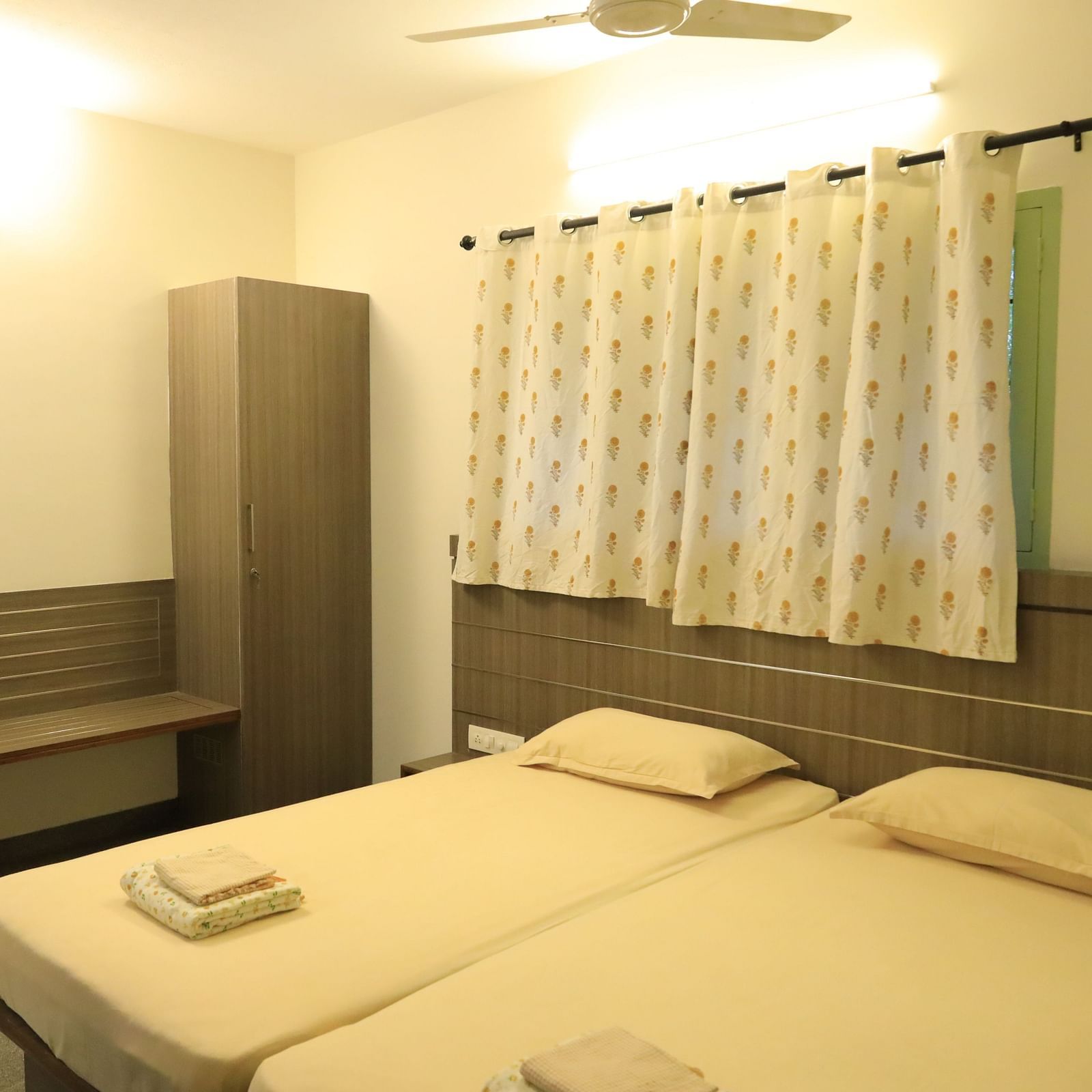 A bedroom at Wyt Hotels Transit Nest, Madurai featuring two single beds, bedside table, and a bench attached to it.