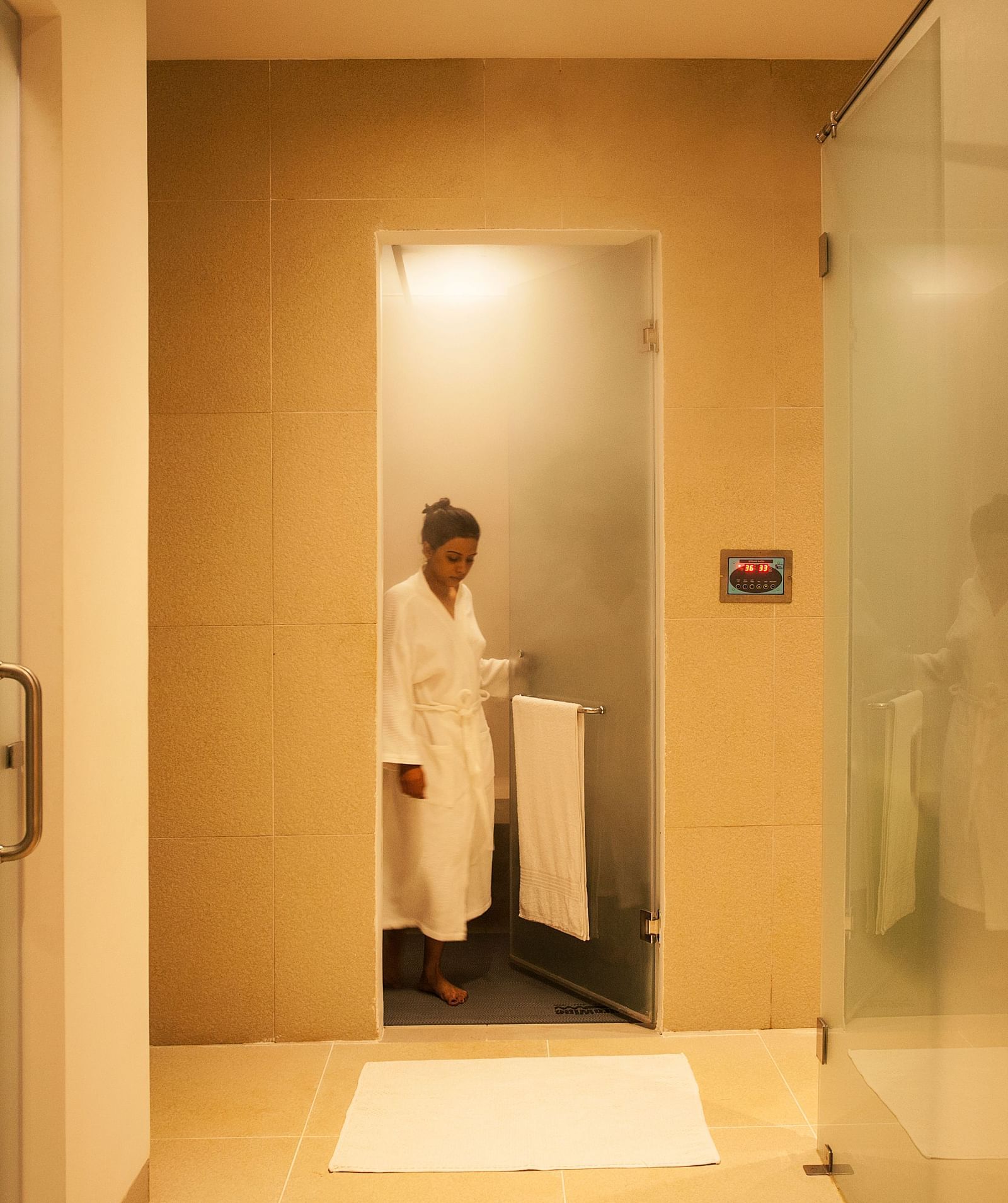 Person in a white robe standing in a shower, glass door, modern bathroom - Shreyas Retreat