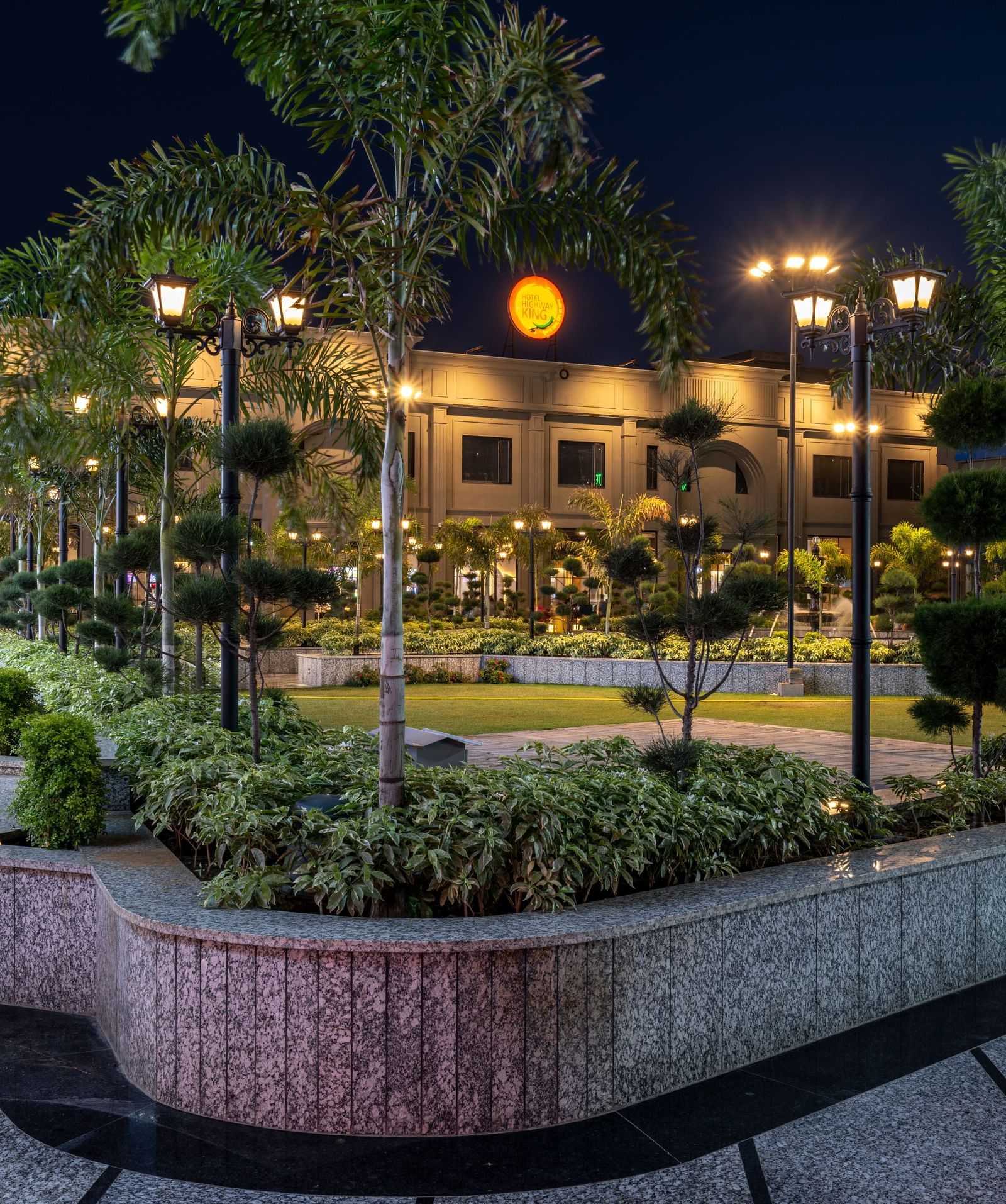 Walkway and landscaped garden at Hotel Highway King, Kishangarh with palm trees and night lighting.