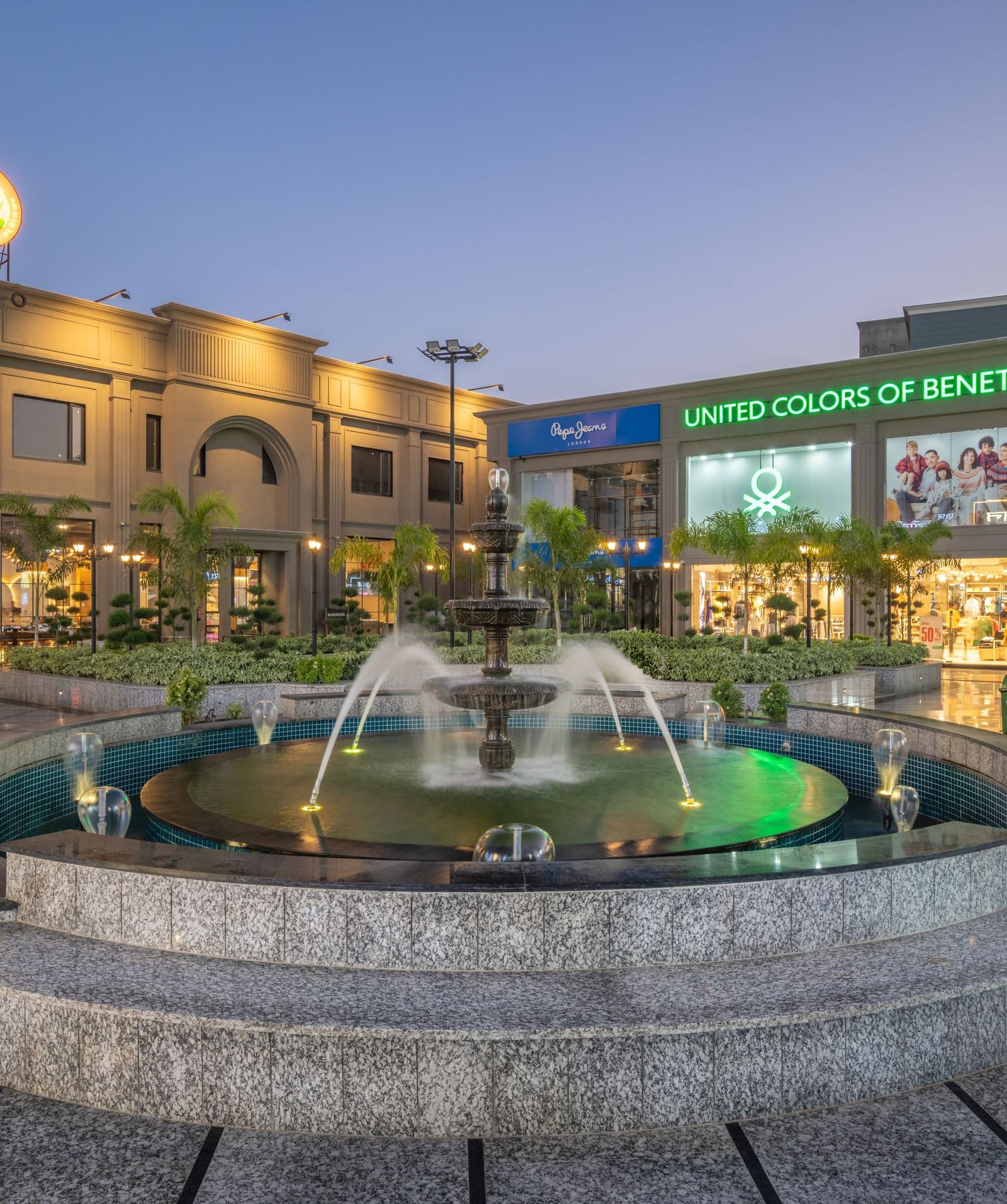 Evening view of fountain and courtyard at Hotel Highway King, Kishangarh with signage and building in the background.