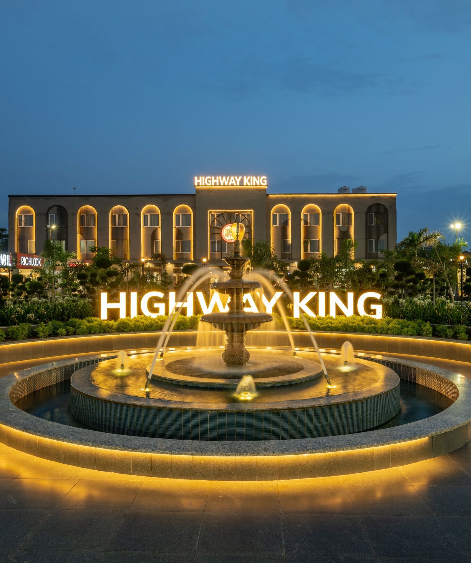 Wide shot of the facade of Hotel Highway King, Neemrana, featuring a fountain and warm lighting that highlights the view against the night sky.