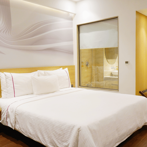 Deluxe room at Nemesia with a king size bed, modern decor, and a stylish en-suite bathroom visible through a glass partition.