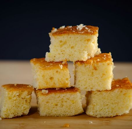 A stack of golden cornbread squares on a flat surface.