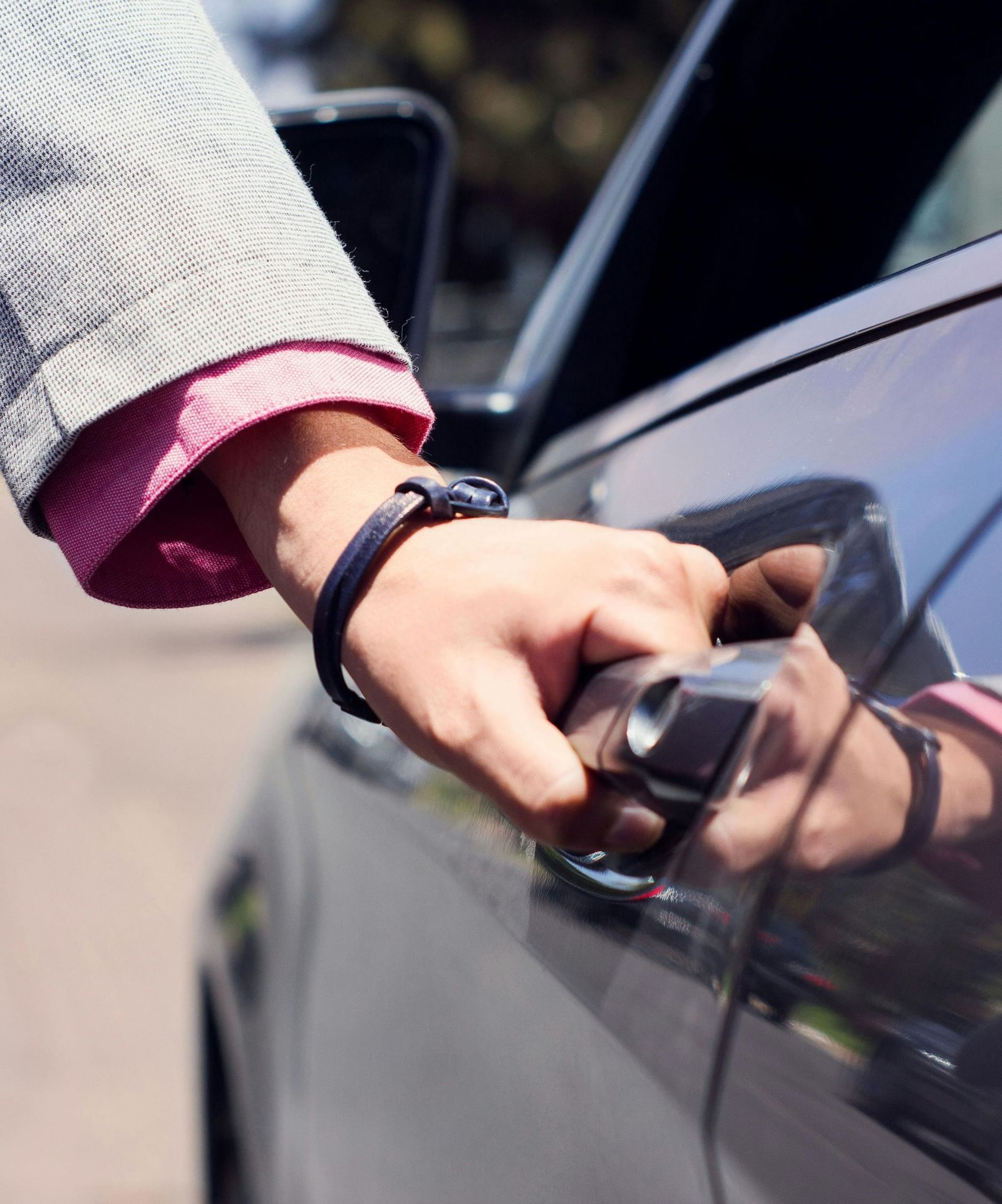  A close-up shot of a person's hand wearing a watch, reaching for the door handle of a dark-coloured car
