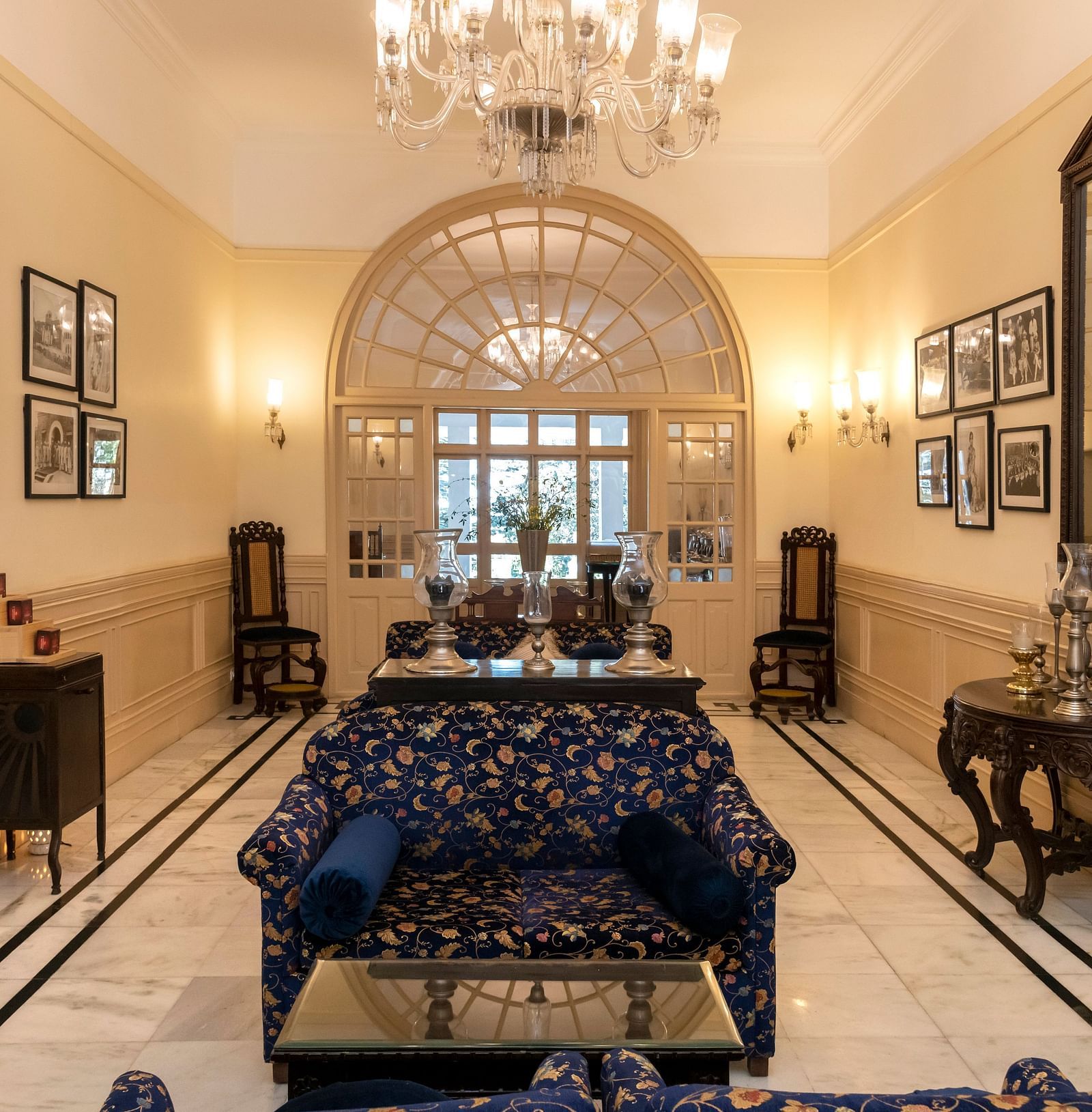 The lobby of The Claridges Nabha Residence in Mussoorie, featuring sofas, wall paintings, a chandelier, a mirror, and various decorative items.