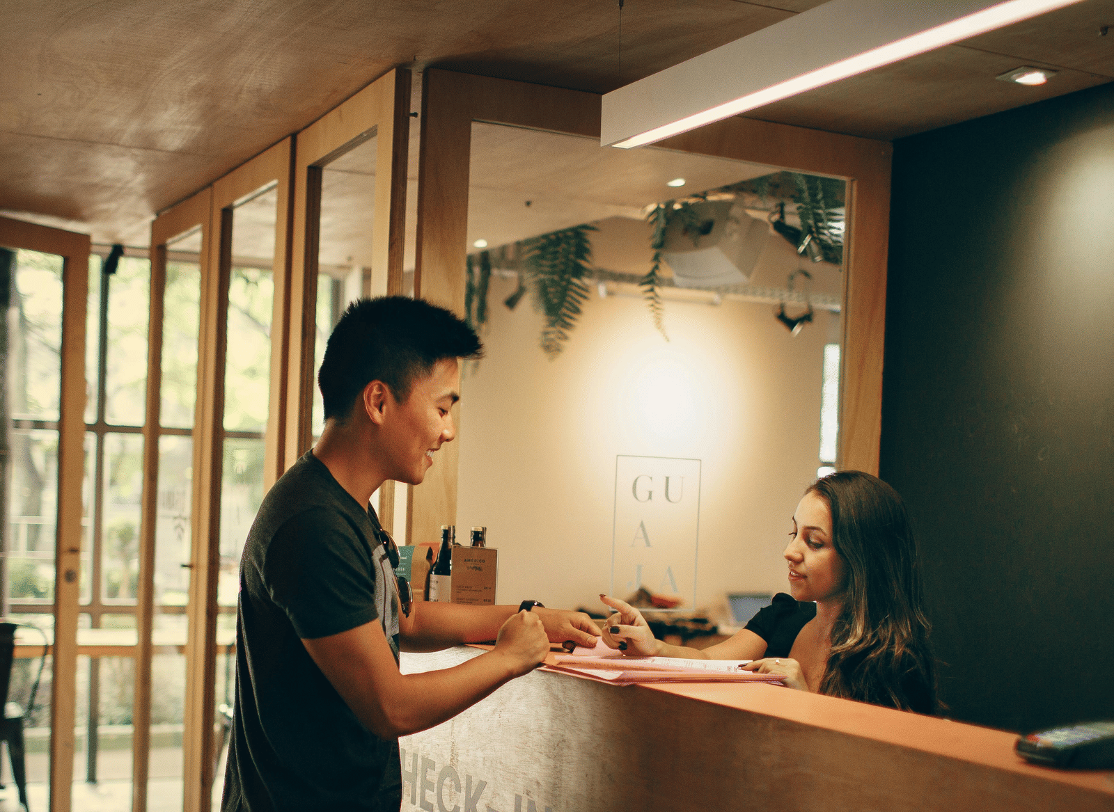A person standing in front of a reception desk in conversation with a woman attending to his queries.
