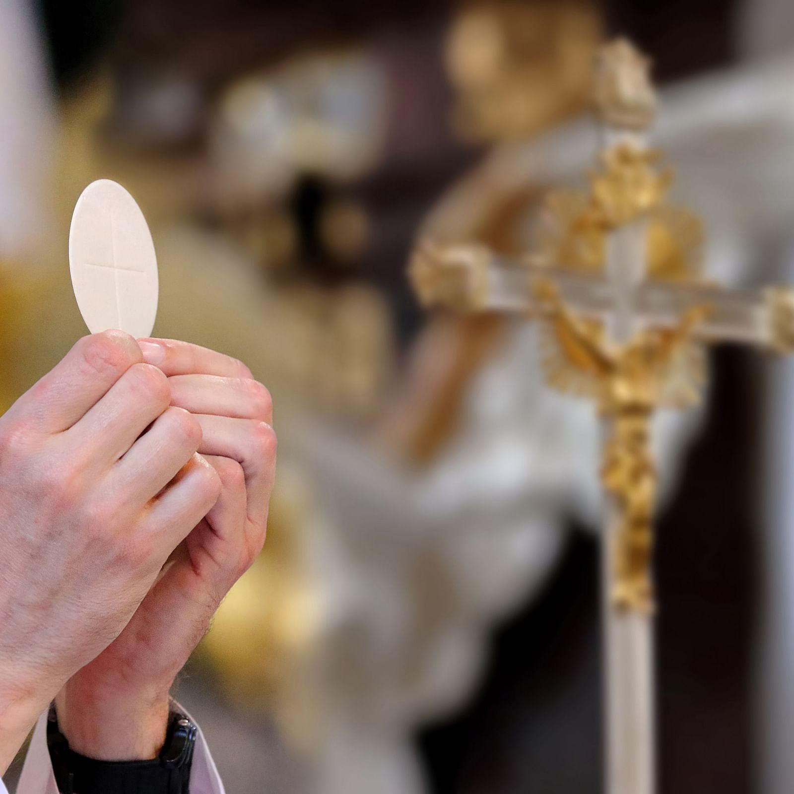 A priest's hands holding up the Communion host during a solemn religious ceremony.