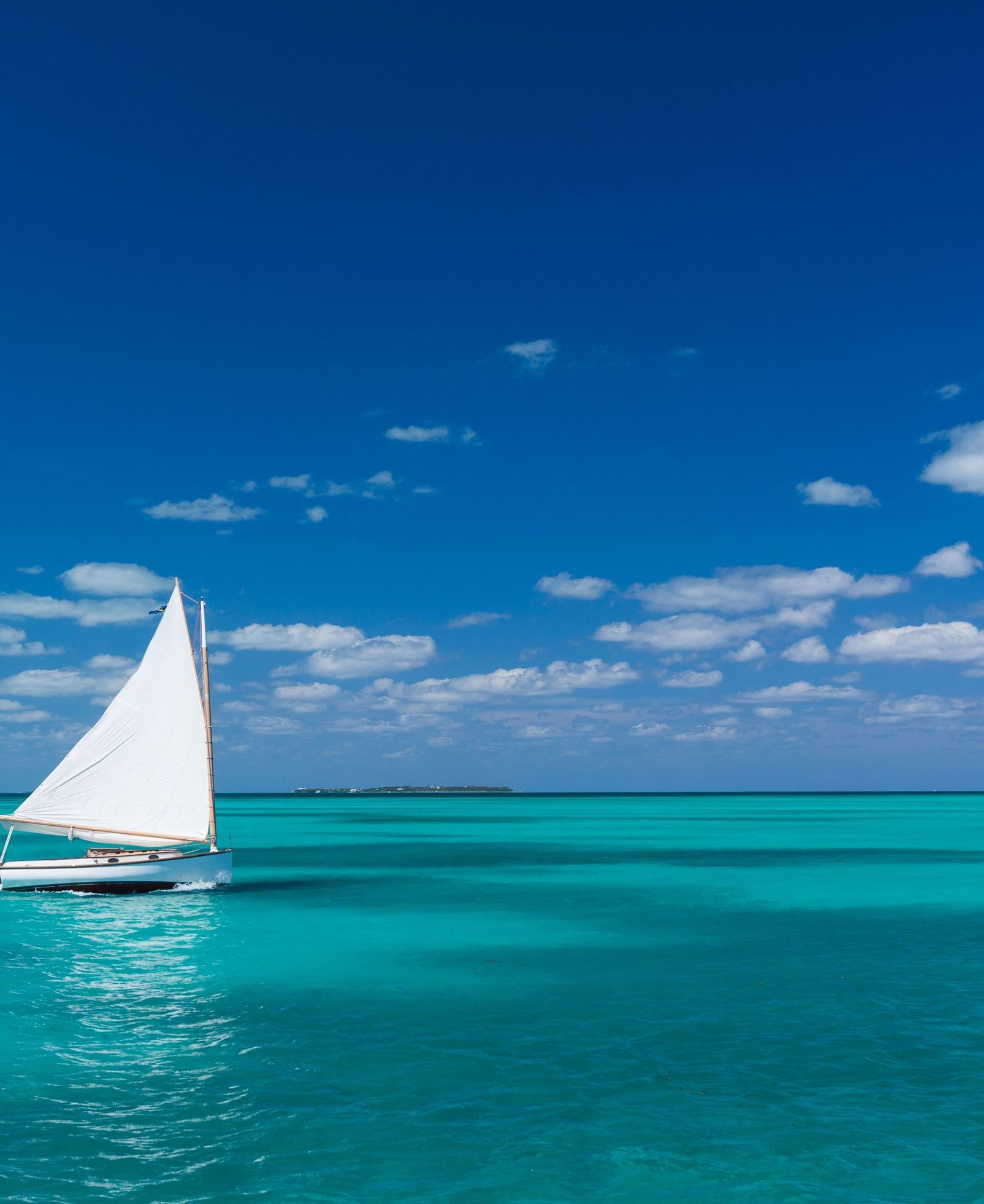 A sailboat gliding across calm turquoise waters under a clear blue sky, with the ocean stretching to the horizon in the background | Abaco Inn