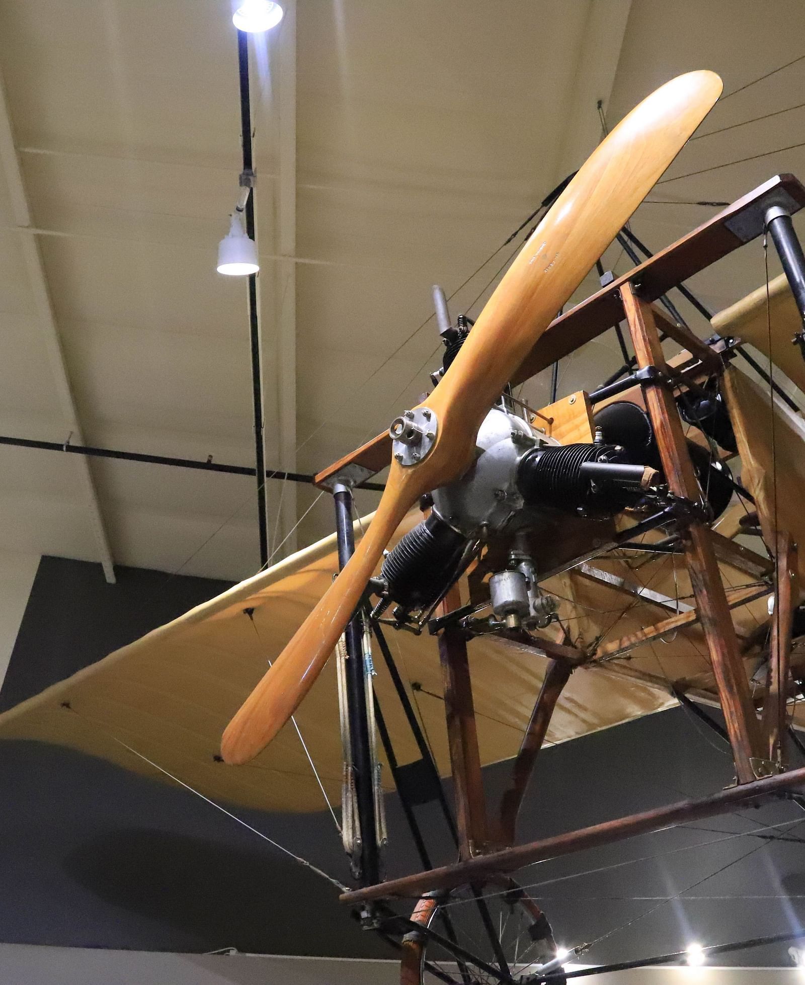 Close-up of a vintage wooden biplane suspended from the ceiling at Hartstone Inn’s aviation-themed exhibit, showcasing its large wooden propeller, radial engine, and fabric-covered wings under overhead lighting