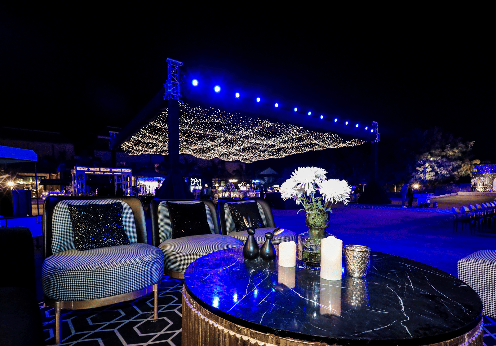 Outdoor lounge setup with round tables and chairs under blue lights at Ananta Spa and Resorts, Jaipur.