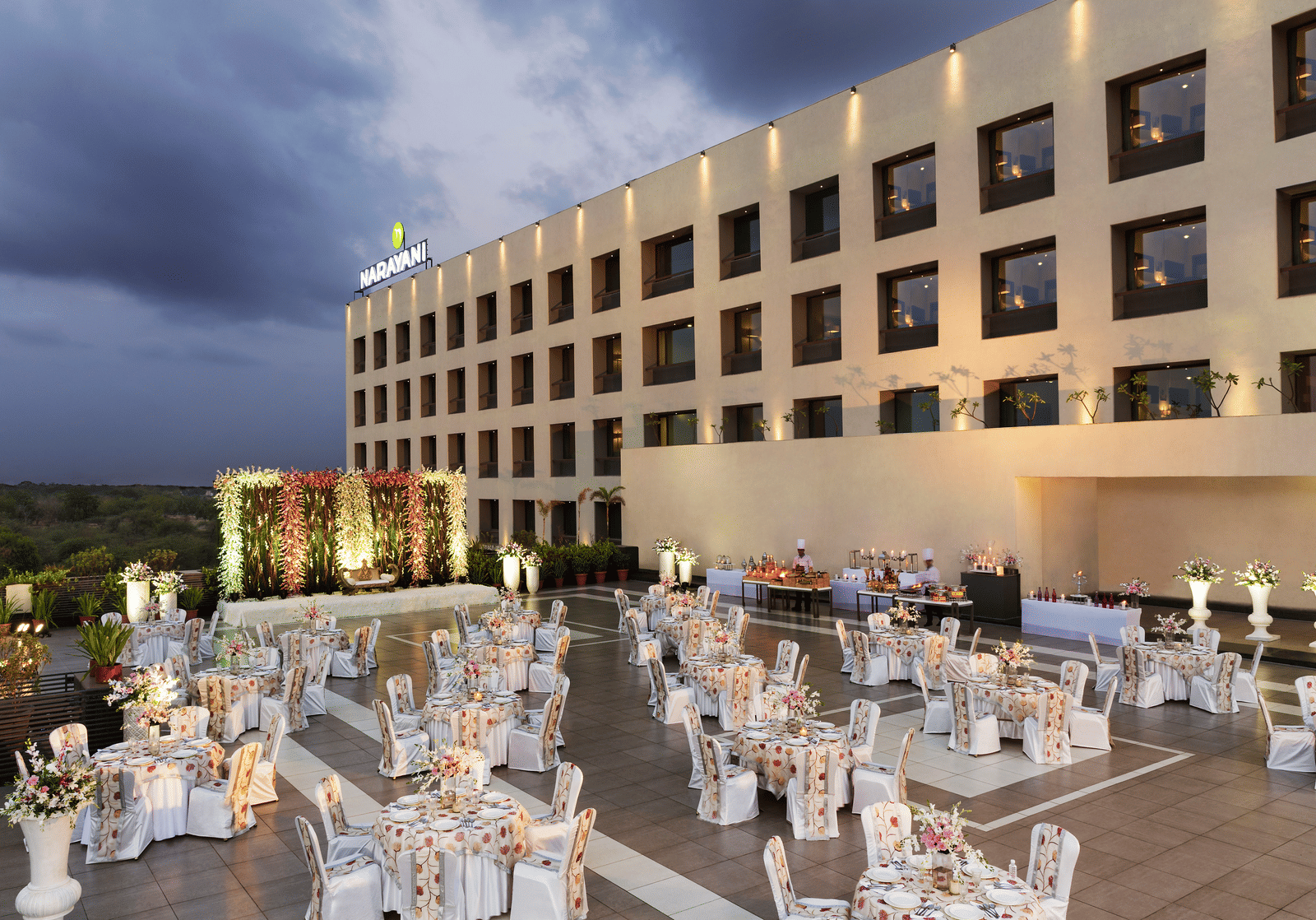 Outdoor banquet setup with white chairs and tables at Narayani Heights Hotel & Resorts, Ahmedabad.