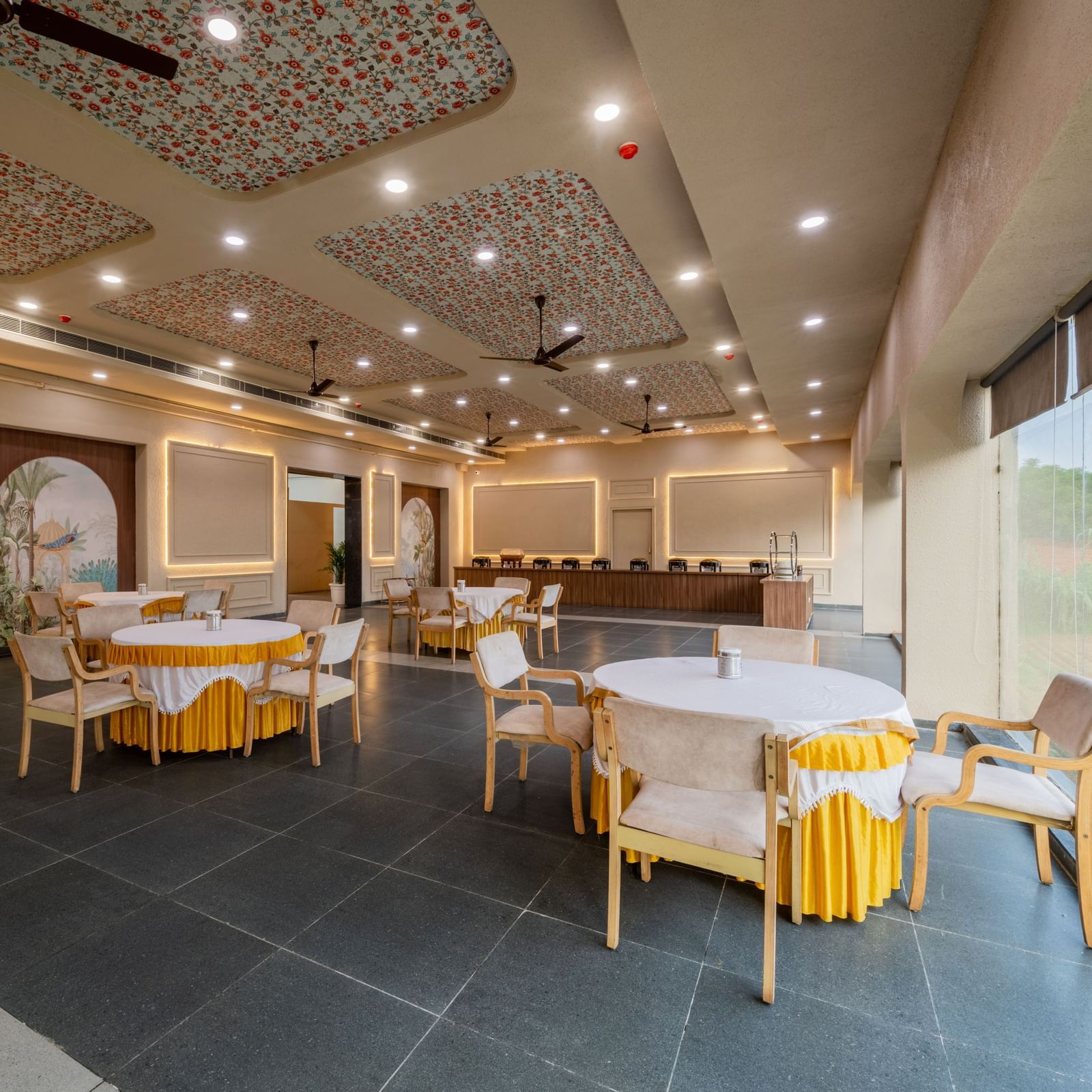 Elegant banquet area with chairs arranged around round tables, featuring large windows at Hotel Highway King, Neemrana. 