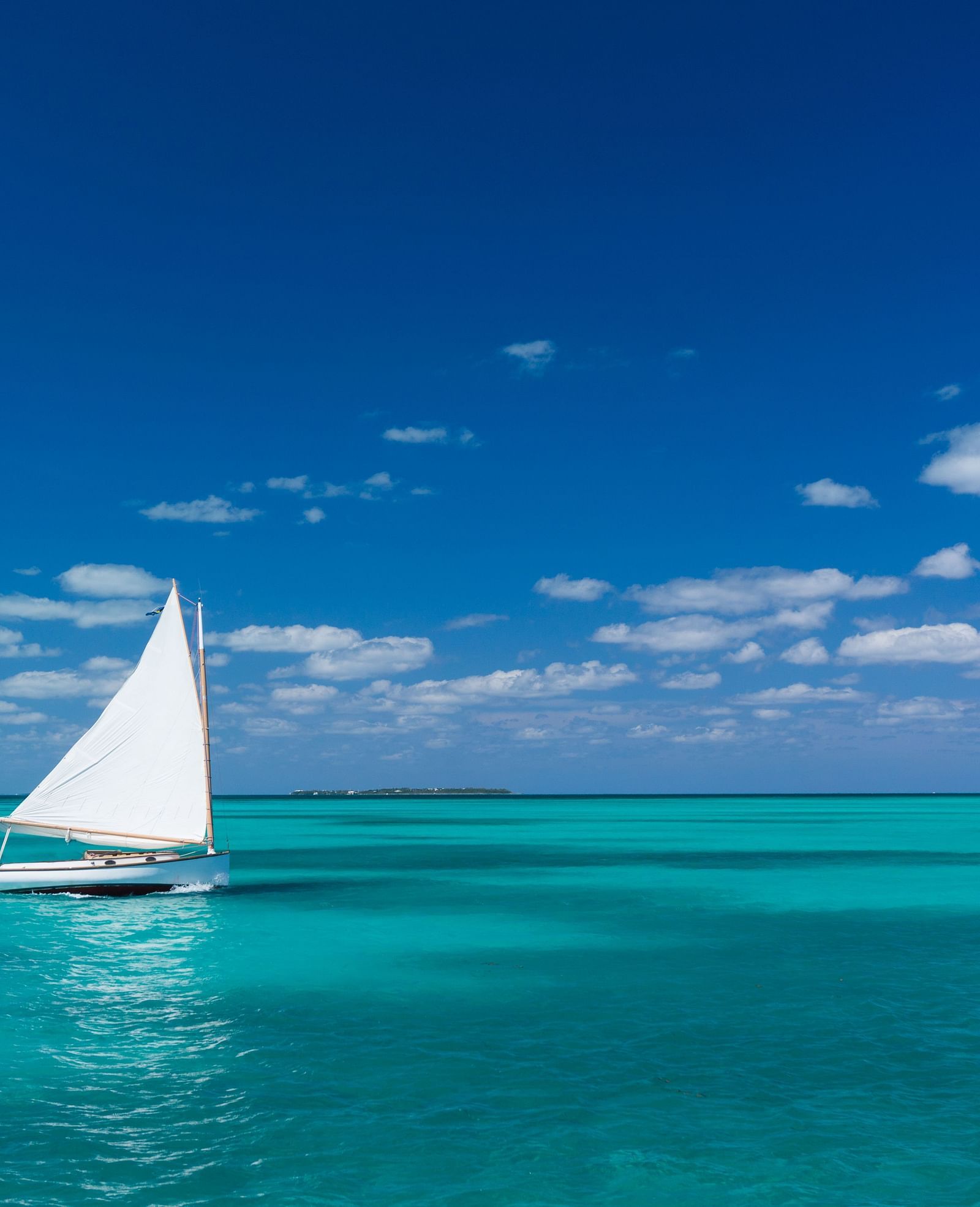 A sailboat gliding across calm turquoise waters under a clear blue sky, with the ocean stretching to the horizon in the background | Abaco Inn