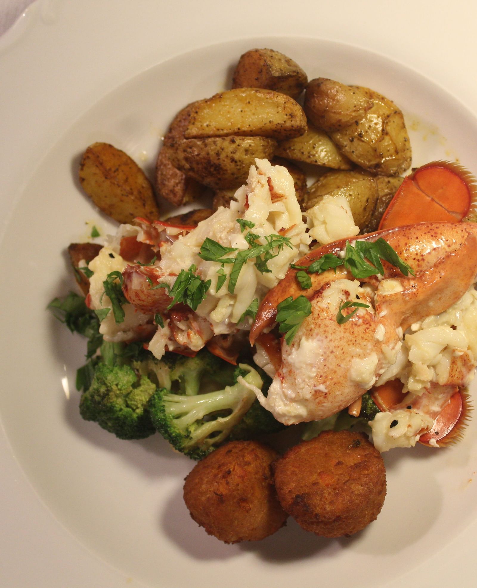 Lobster served with potatoes, greens, and vegetables on a white plate.