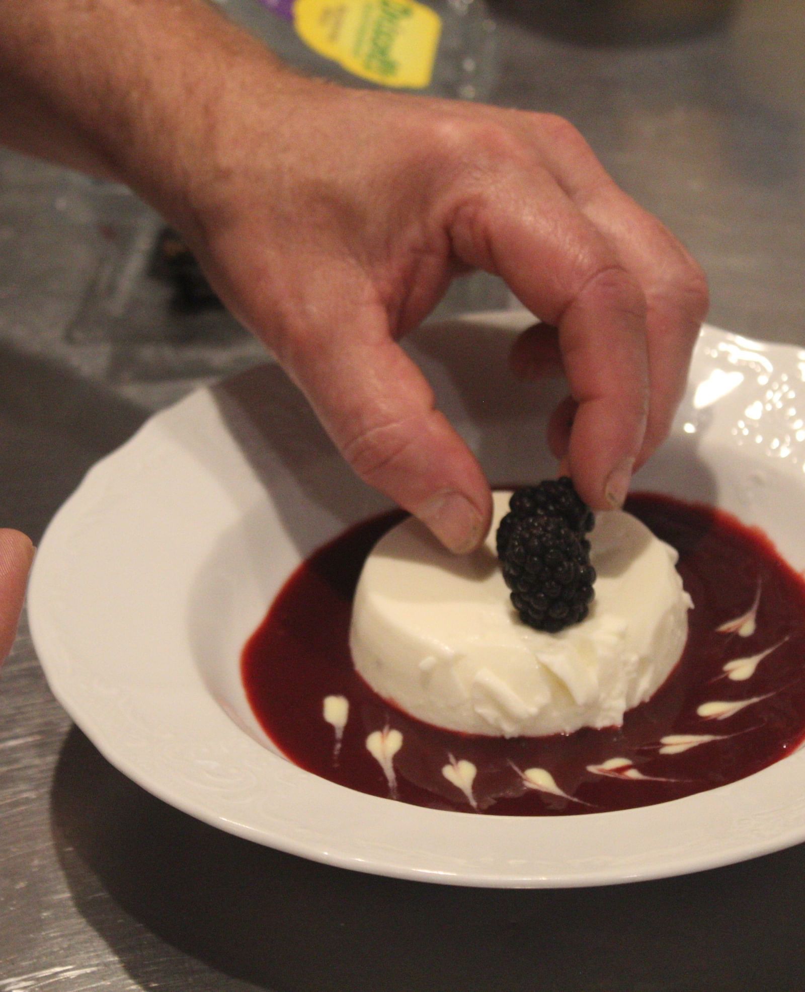 A hand placing garnish on a plated dessert with berry sauce.