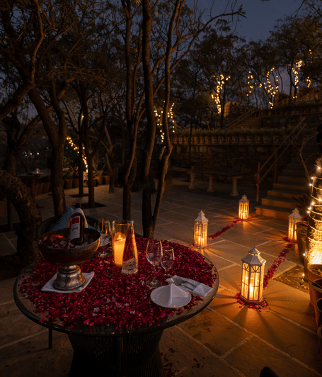 Romantic candlelit dining setup with a beautifully dressed table surrounded by illuminated trees and lanterns in a garden setting | YAAN Udaipur