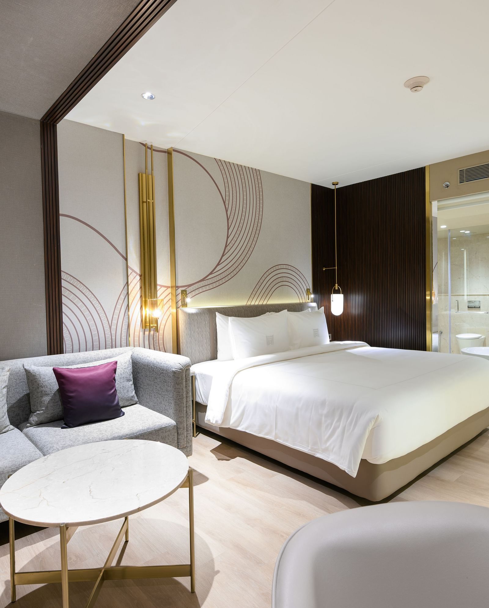 A comfortable hotel room with a large bed, a sofa seating area, and tasteful decor creating a relaxing ambience at Merlis Hotel, Coimbatore.